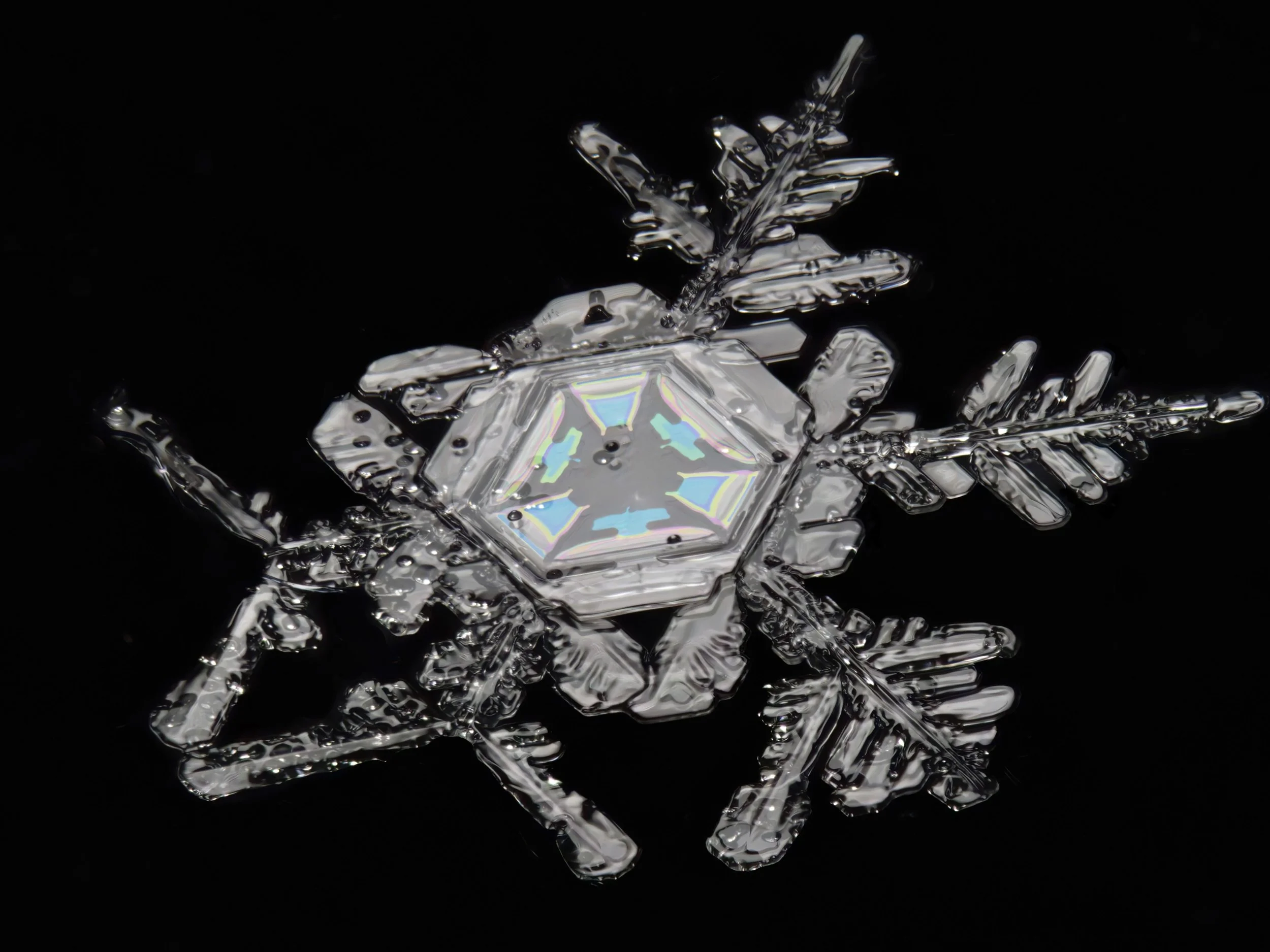 Macro photograph of a snow crystal with a colourful, hexagonal-shaped center and irregular branches.