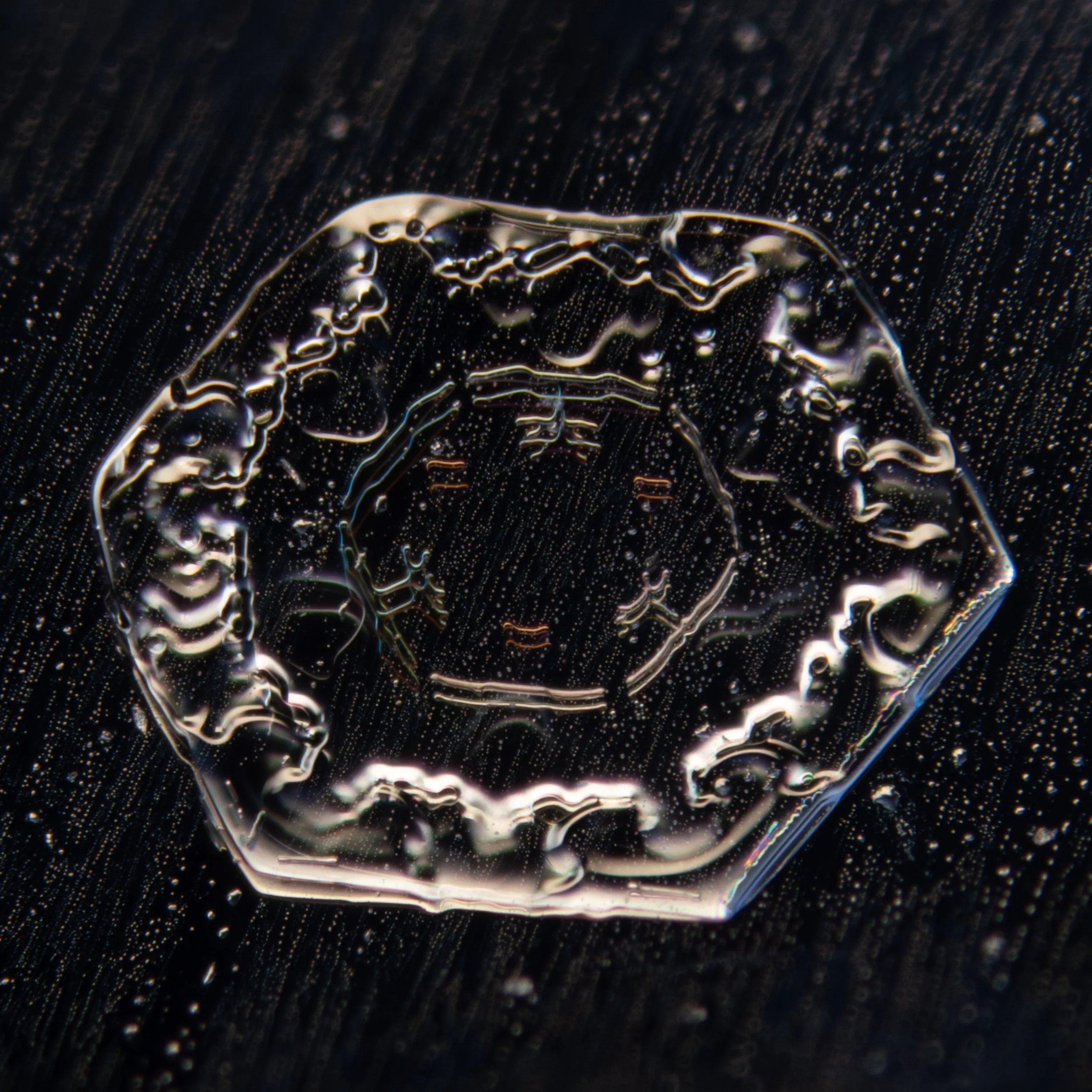 Macro photograph of a simple plate snowflake with prismatic color refraction.