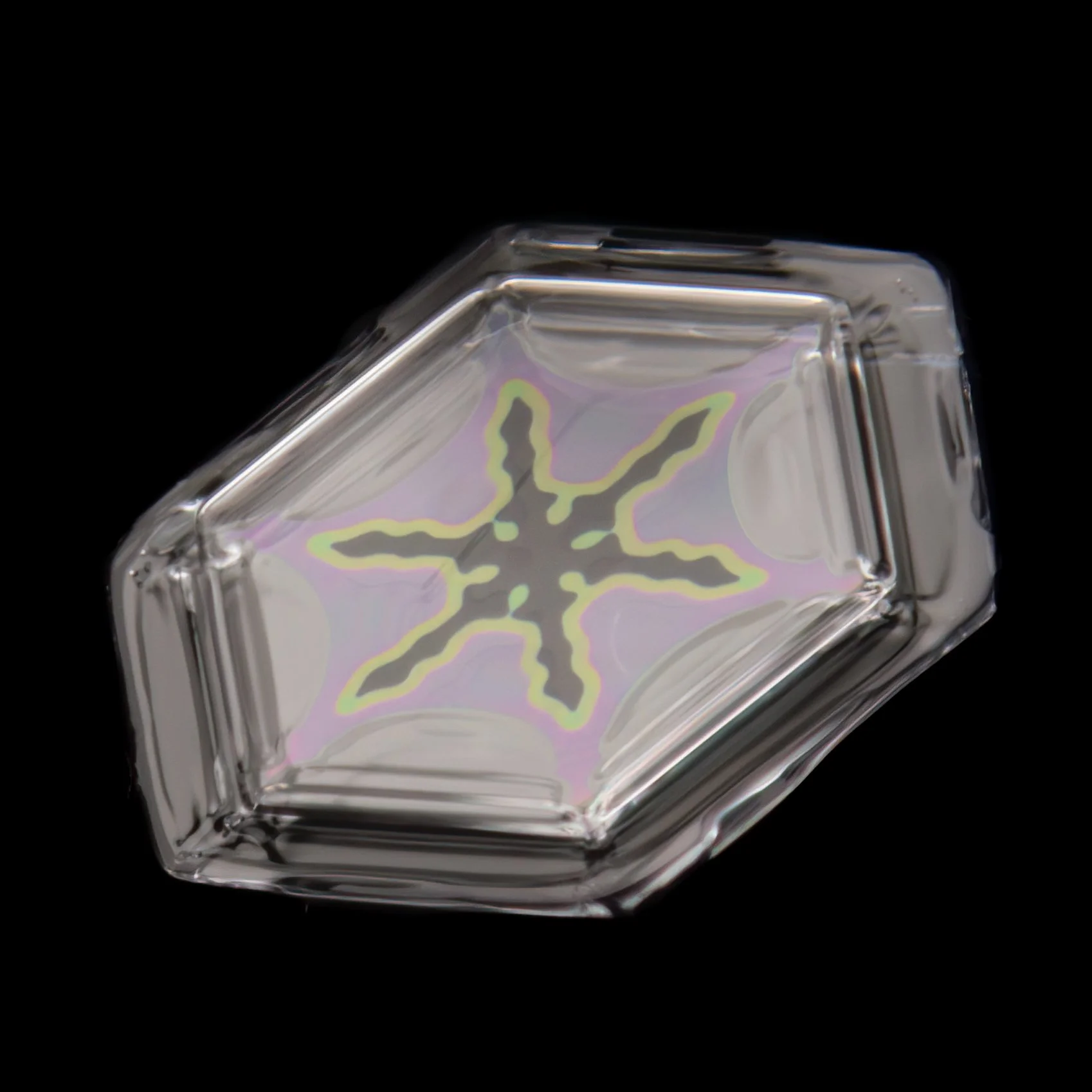 Macro photograph of a small plate snow crystal with visible color refraction and intricate pattern.