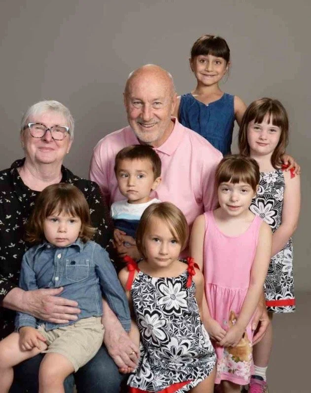 A multi-generational family portrait featuring three elderly adults and five children posing against a plain background.
