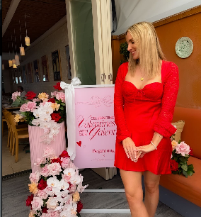 A woman in a red dress standing next to a decorated floral display at a venue, possibly for a special event or celebration.