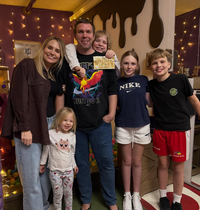 Family of six posing indoors at a recreational facility, with a ball pit in the background and warm lighting.