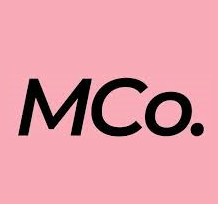 Pink background with black text reading 'MCo.'