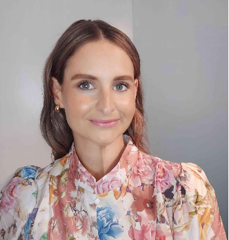 Portrait of a woman with brown hair and blue eyes, wearing a floral blouse with pastel colors, smiling at the camera.