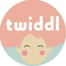 Circular logo with a pink background, featuring a cartoon baby face with closed eyes and a smile, and the word 'twiddl' in white lowercase letters above the baby.