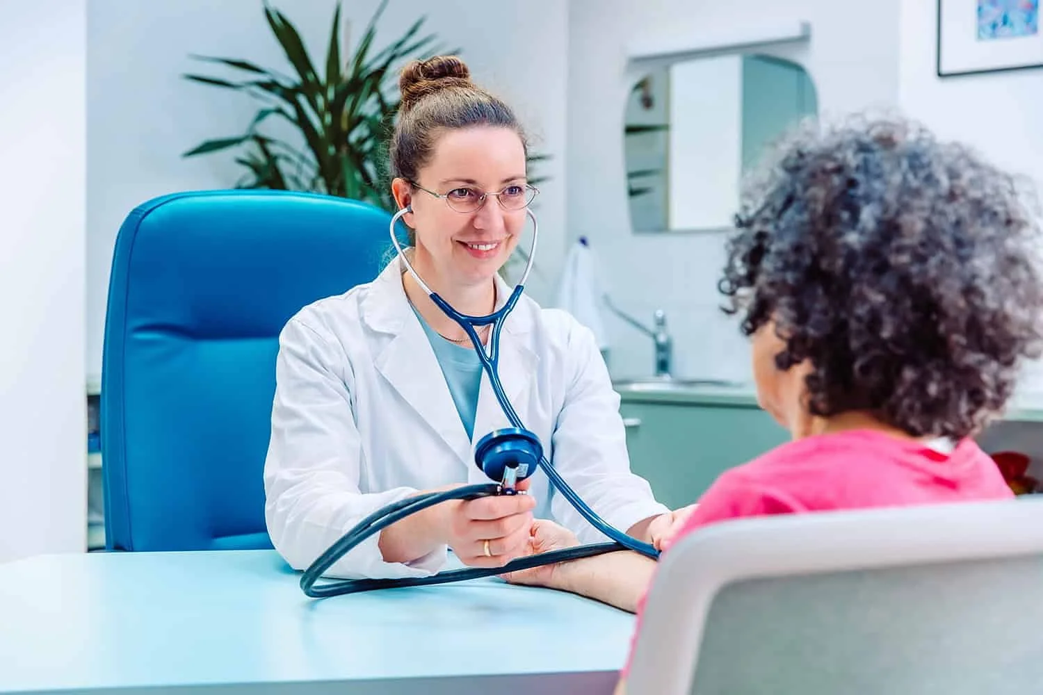 Ärztin mit Stethoskop, die eine Patientin im Krankenzimmer untersucht.