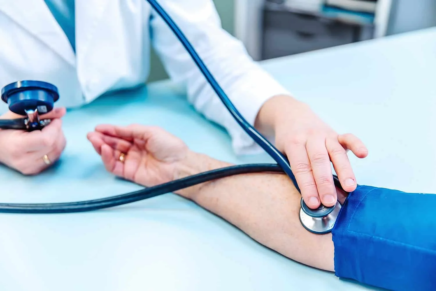 Ein Arzt legt bei einem Patienten mit einem Stethoskop die Hand auf den Arm, um den Puls zu fühlen.