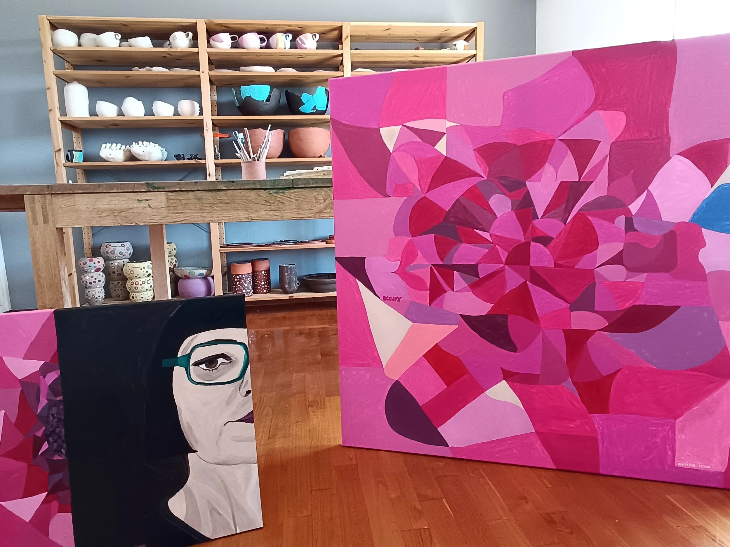 View of a display shelf with ceramics and two paintings from the Neon Dreams series by artist Marisa Iona in her creative space in Volos, Greece.