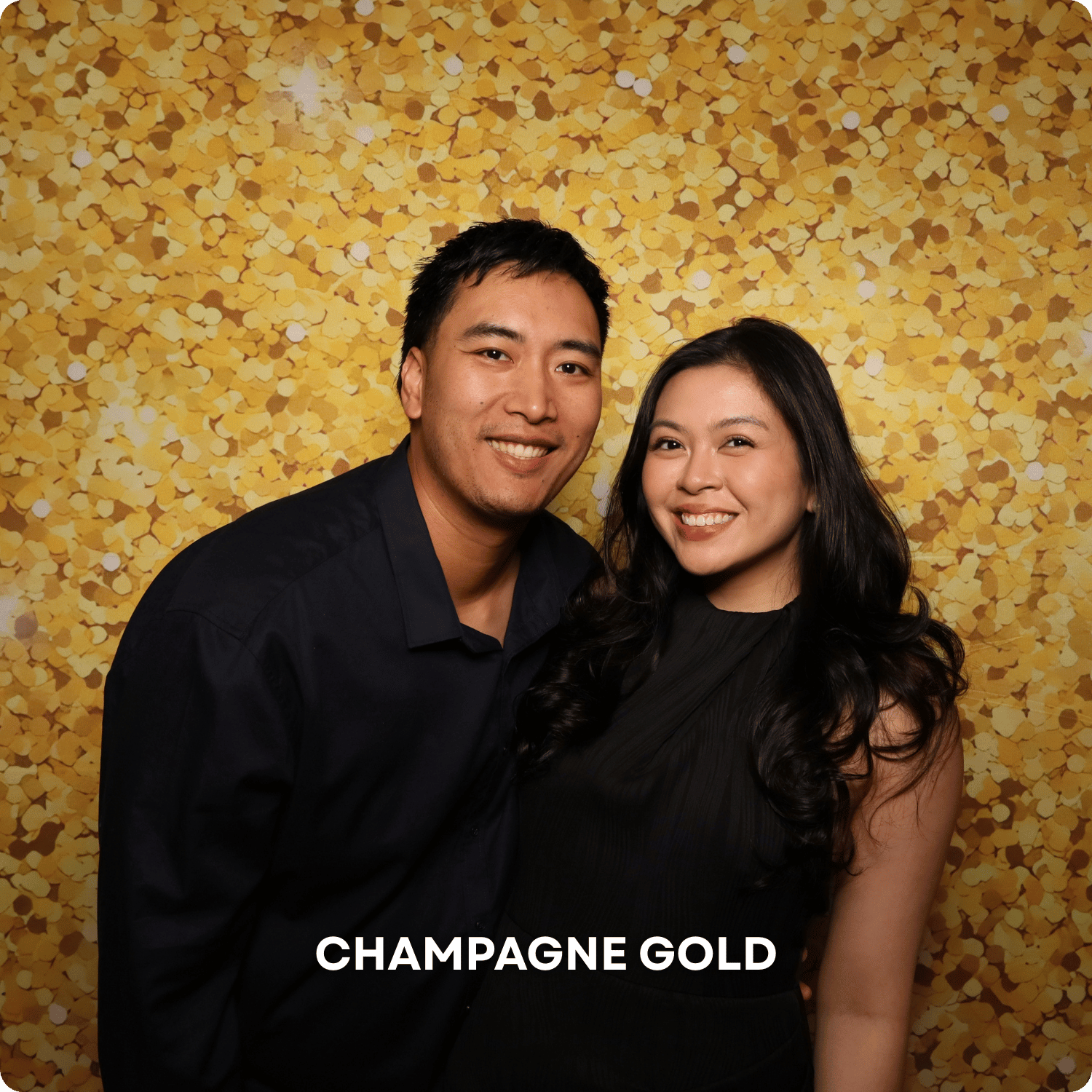 A man and woman smiling posing together in front of a gold confetti backdrop at an event with the text 'CHAMPAGNE GOLD' at the bottom.