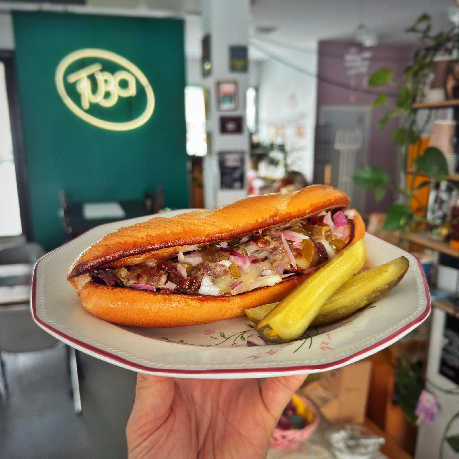 Hot Dog -hot dog ilman sinileipää, täytetty paloilla leikatuilla liha- ja vihannestäytteillä ja päällystetty sinapilla ja säilykkeillä, tarjoiltuna pienellä lautasella ja lisukkeena suolakurkkuja.
