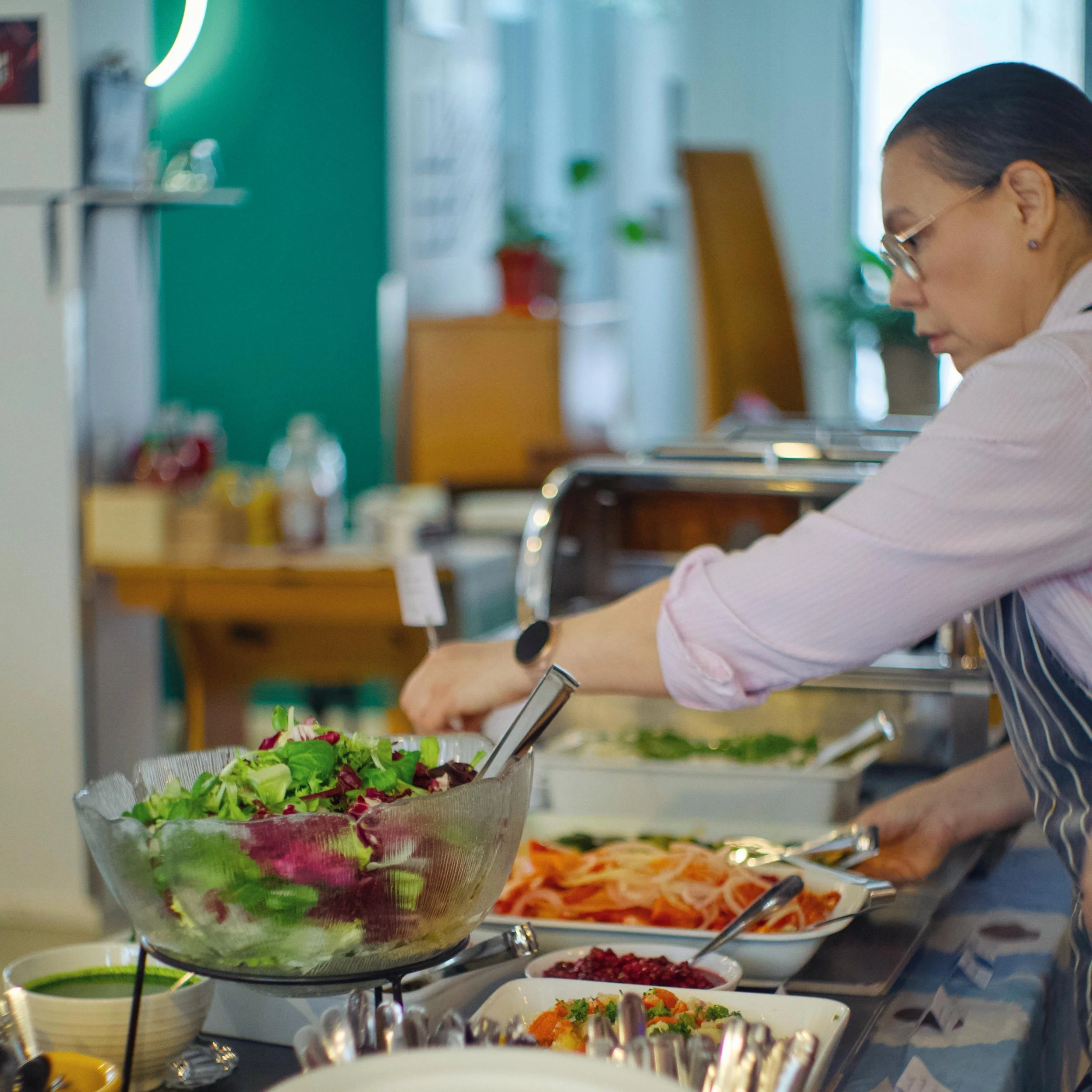 Nainen valmistelee salaattia buffetpöydässä.
