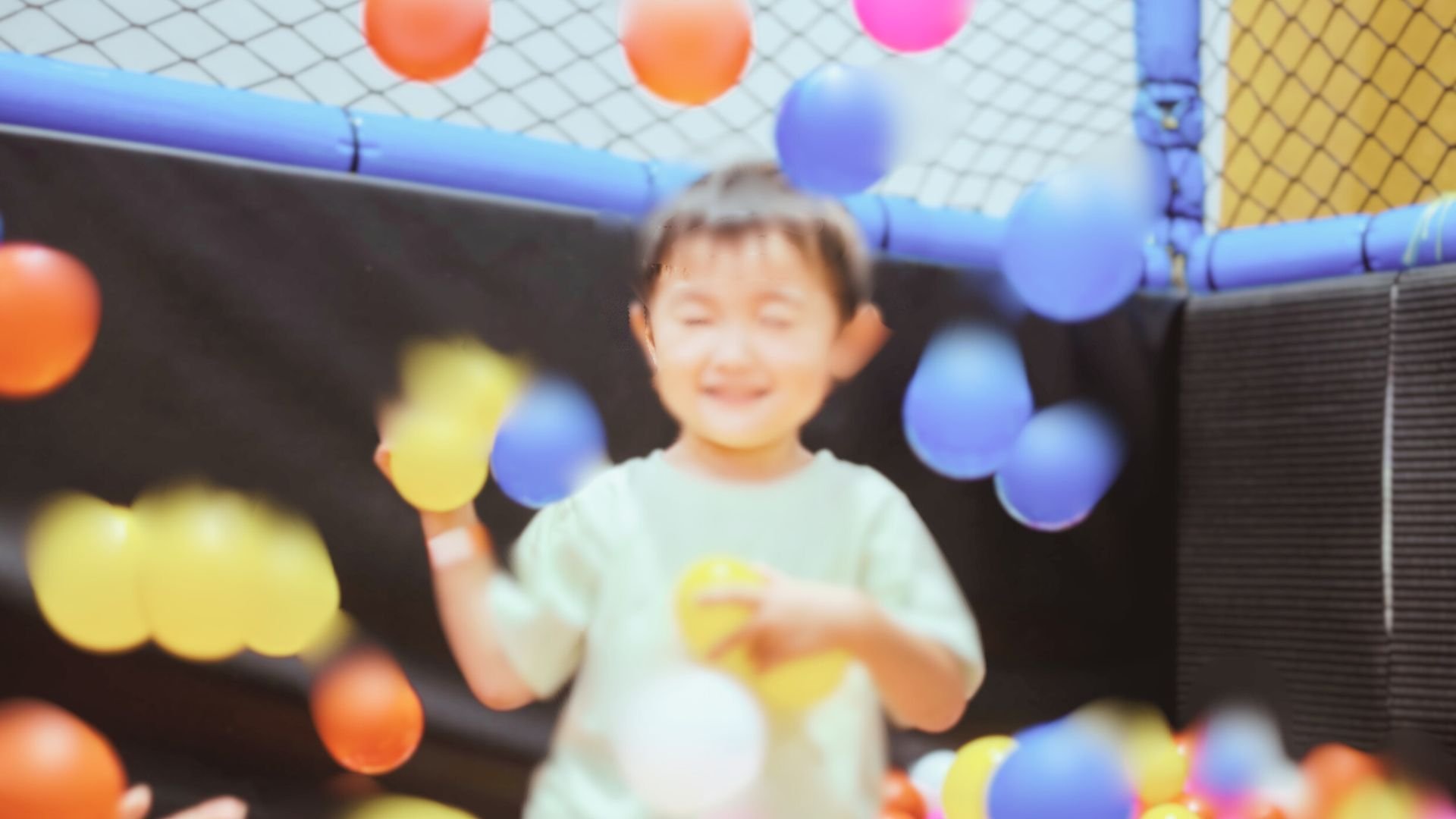 A young boy with a big smile playing in a ball pit filled with colorful plastic balls at an indoor play area.