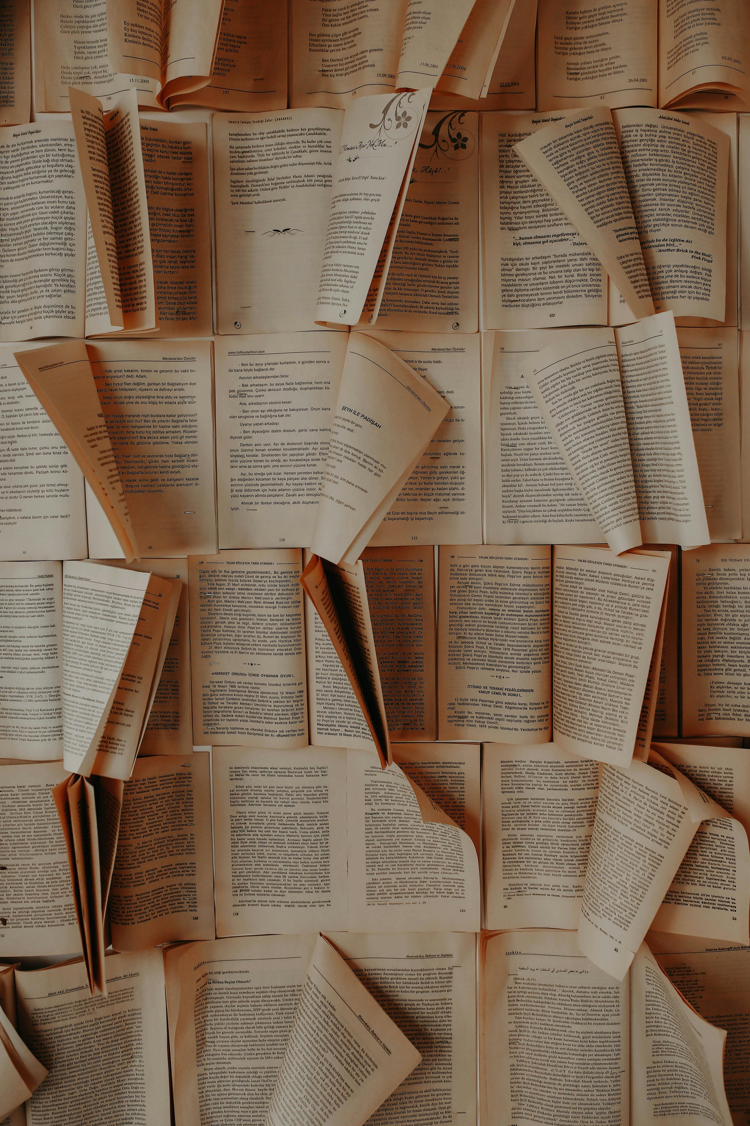 A close-up view of several open books with pages fanned out, arranged in a grid pattern, creating a textured background.