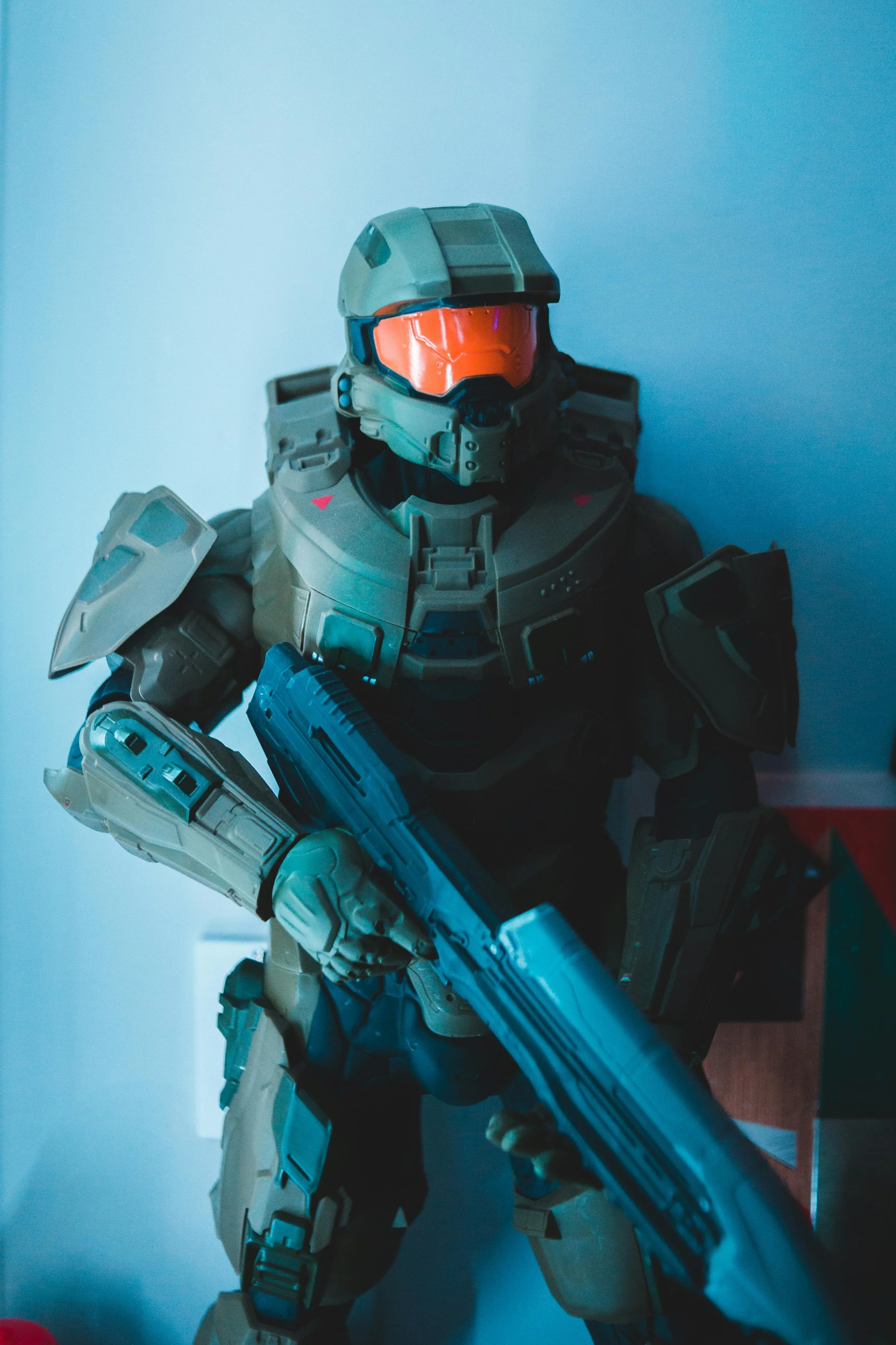 A detailed action figure of a futuristic soldier in tan armor with a helmet featuring an orange visor, holding a large weapon, in a blue-lit environment.