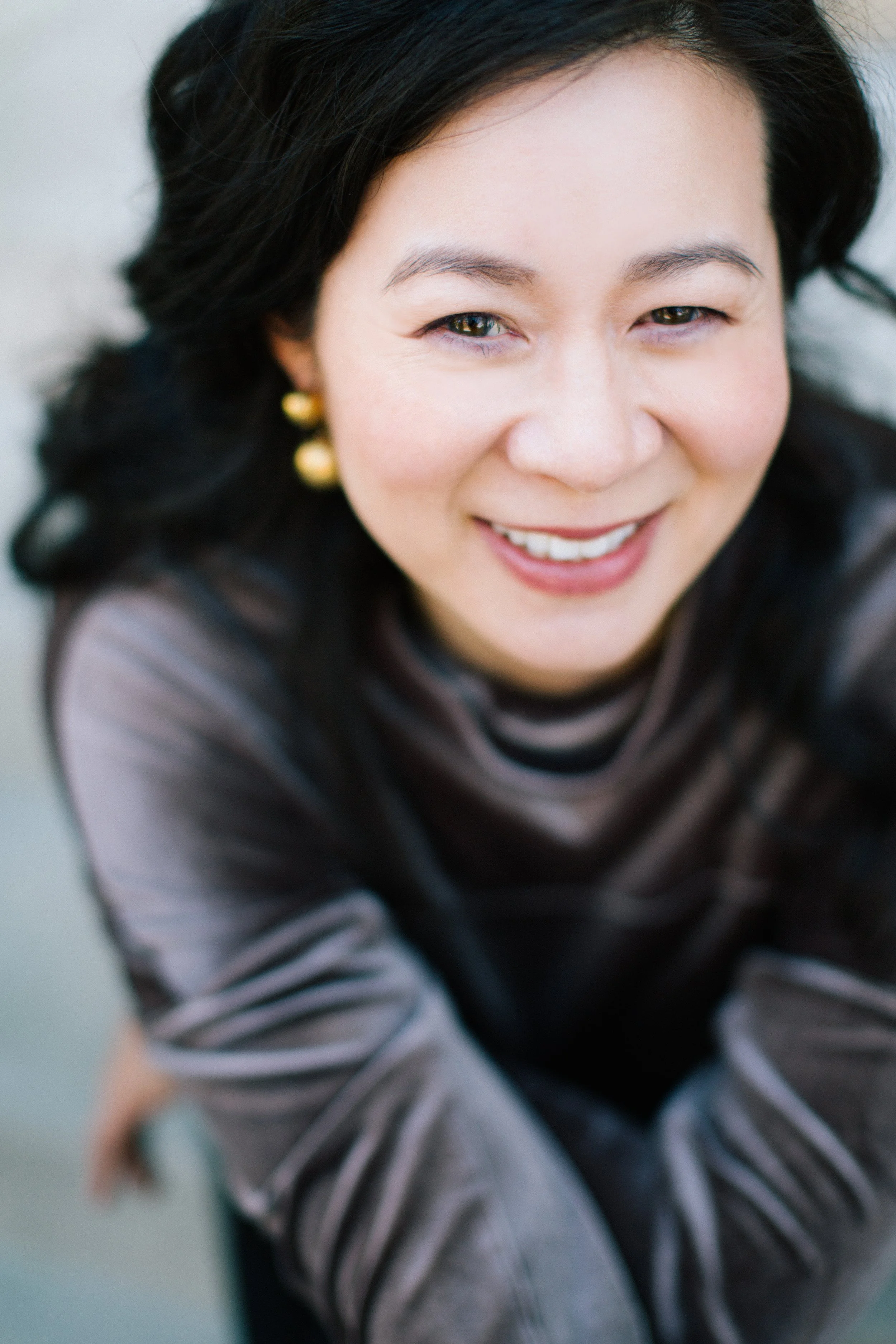 Cindy Kay with dark hair and earrings, wearing a striped top, looking up at the camera.