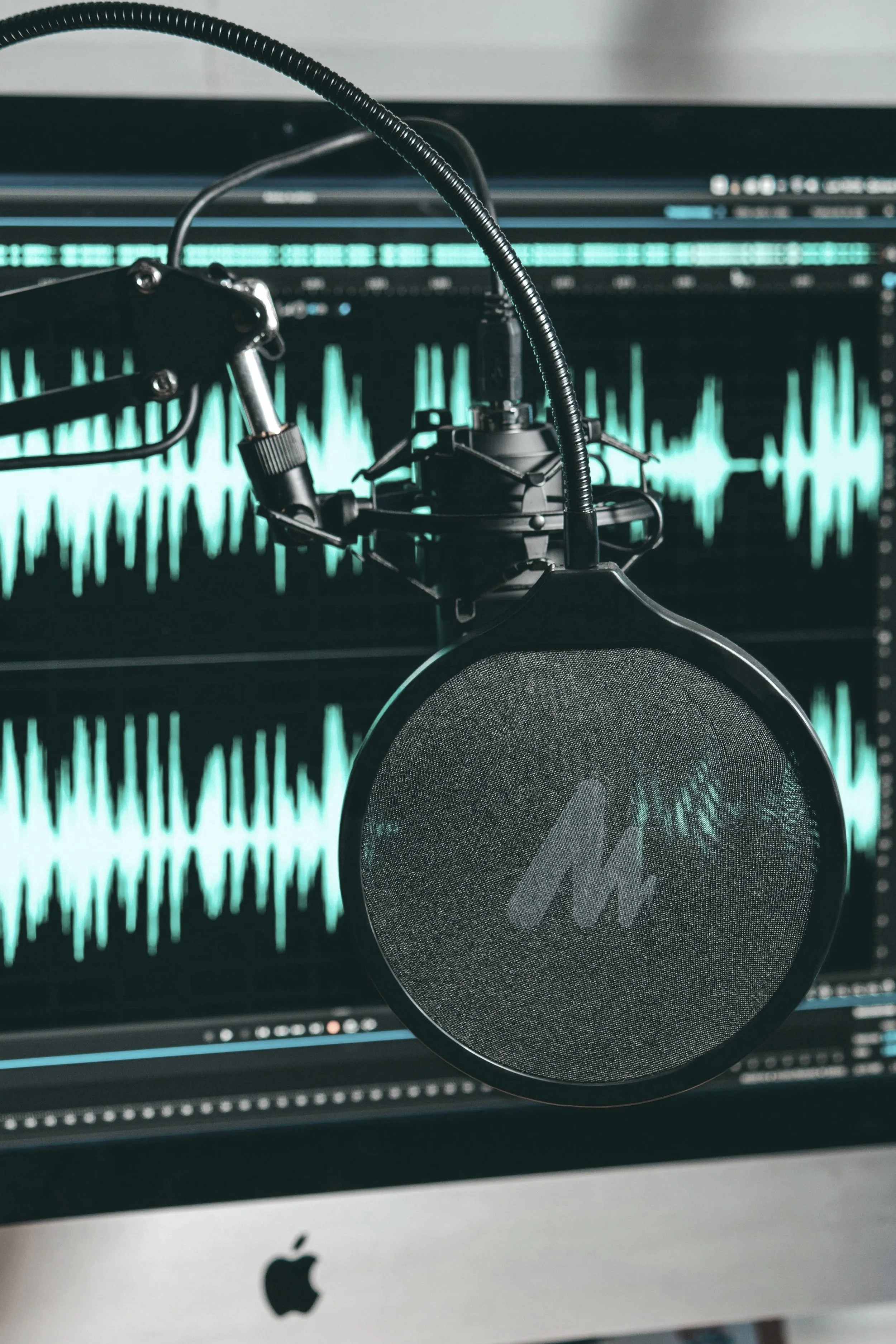 Microphone in front of audio editing software display on an Apple computer.