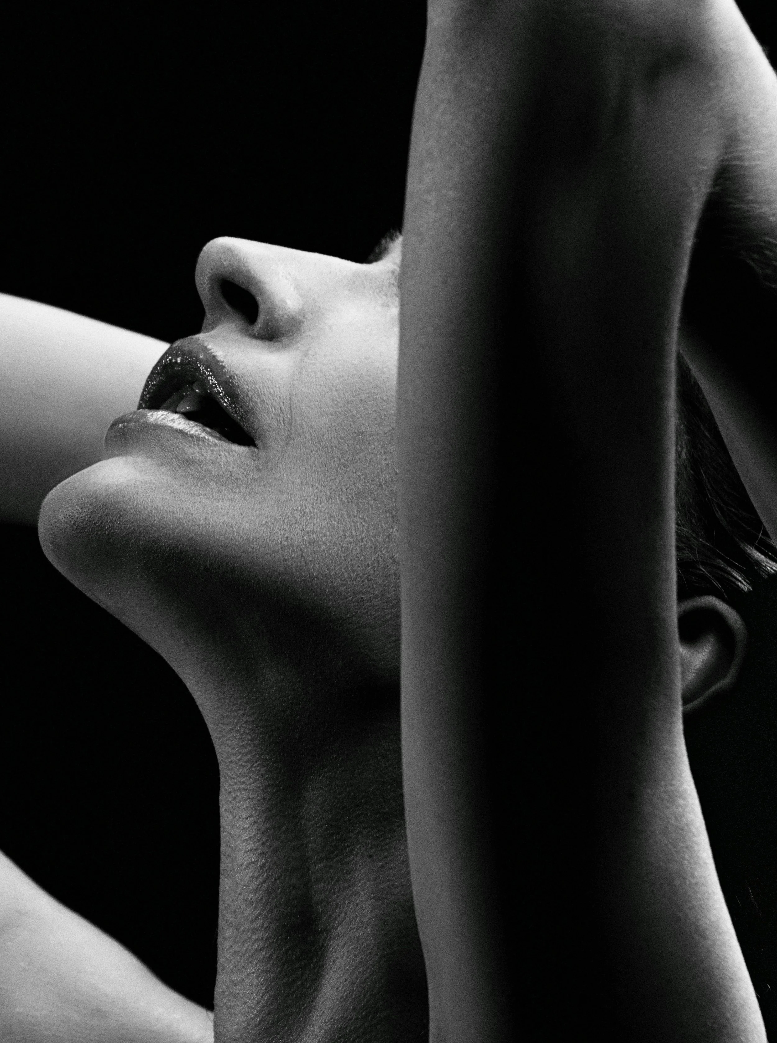 Close-up black and white photo of a woman's face with eyes closed, head tilted back, and her hand covering part of her face.