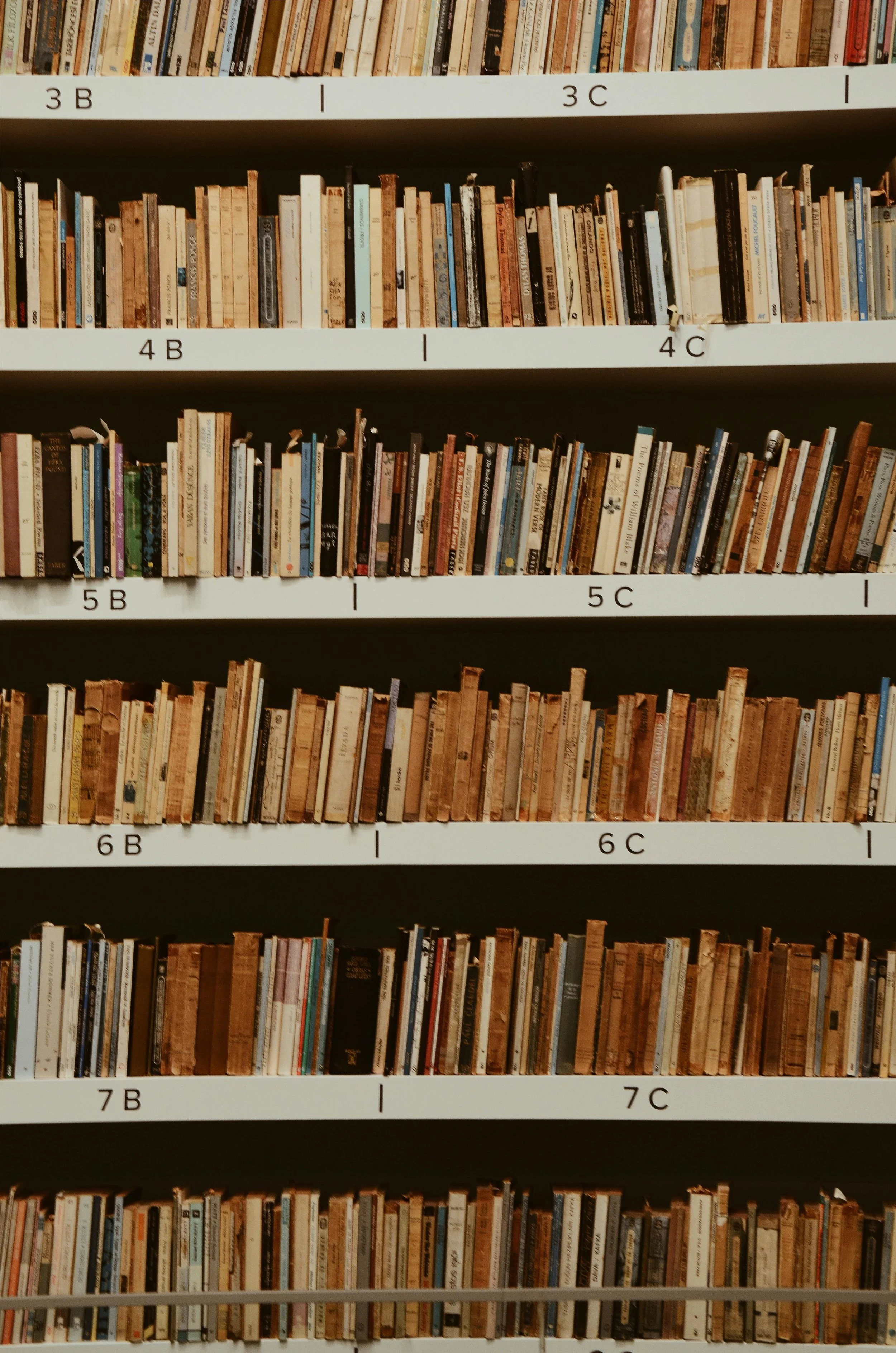 Multiple shelves filled with books in a library, labeled with letter and number codes.