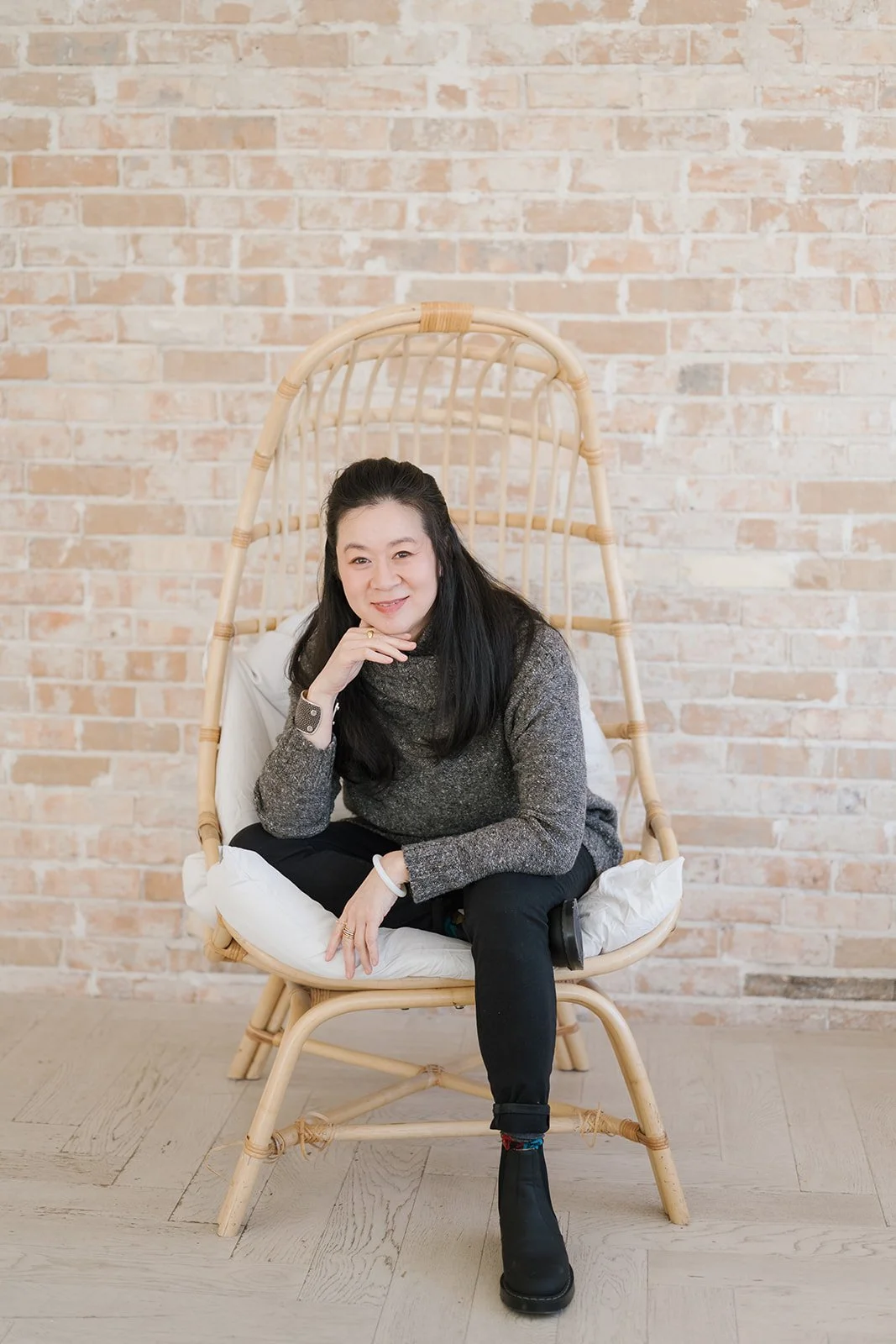 Cindy Kay sitting on a rattan chair with a brick wall background.