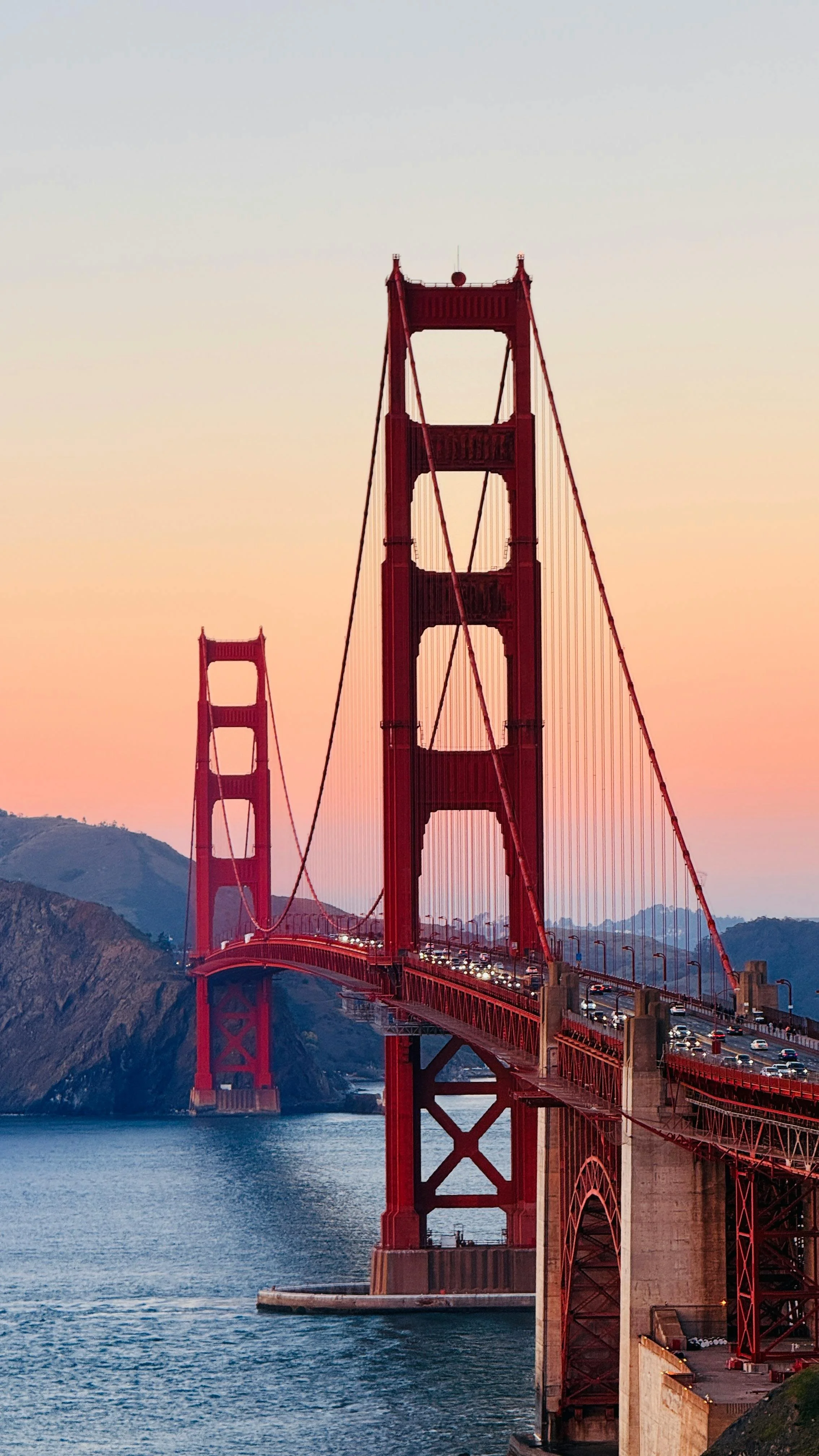 Golden Gate Bridge during sunset with cars on the bridge and hilly landscape in the background.