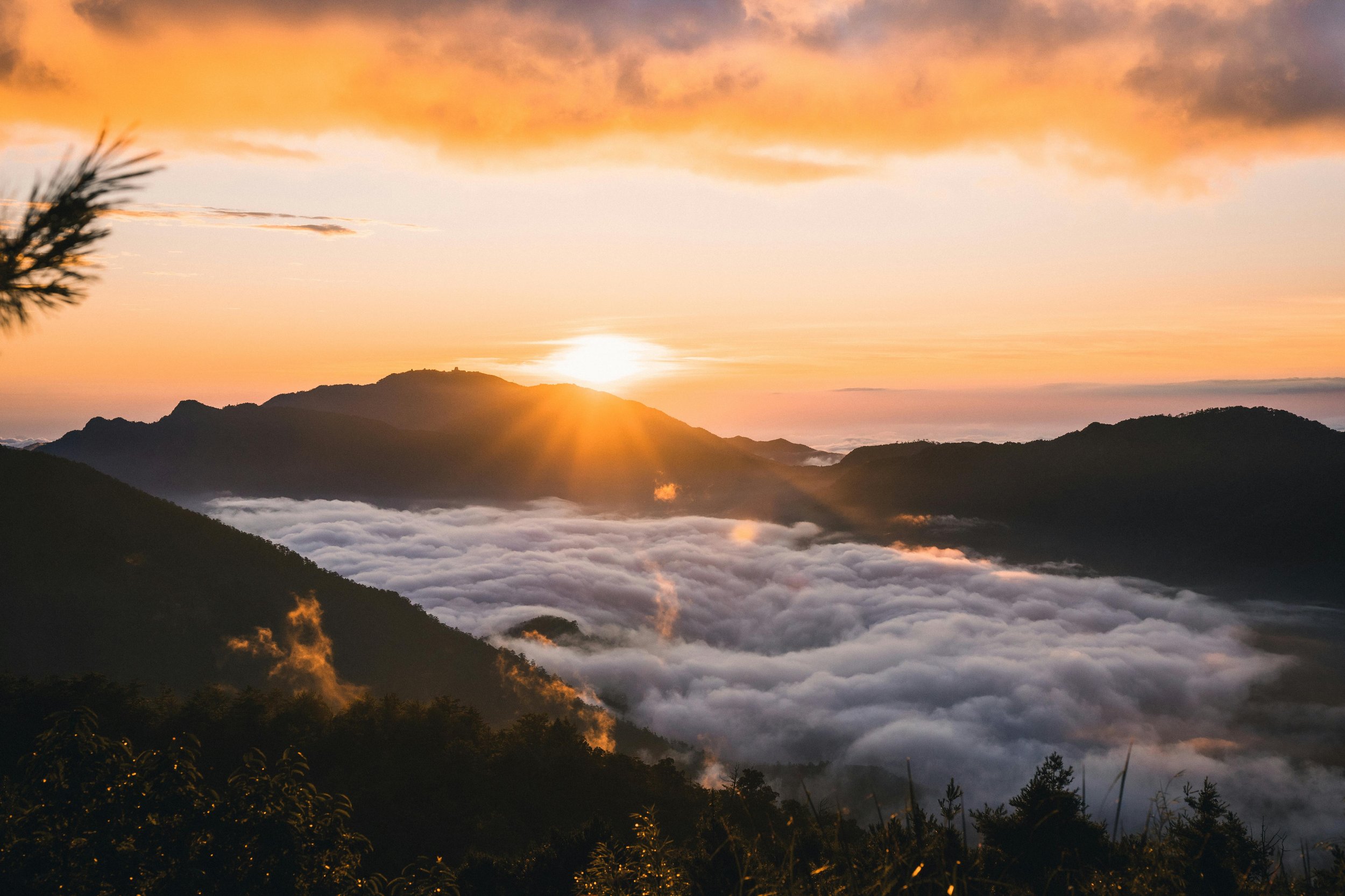 Sunrise over mountains with a cloud-filled valley, orange and pink sky, and some fog rising from the hills.