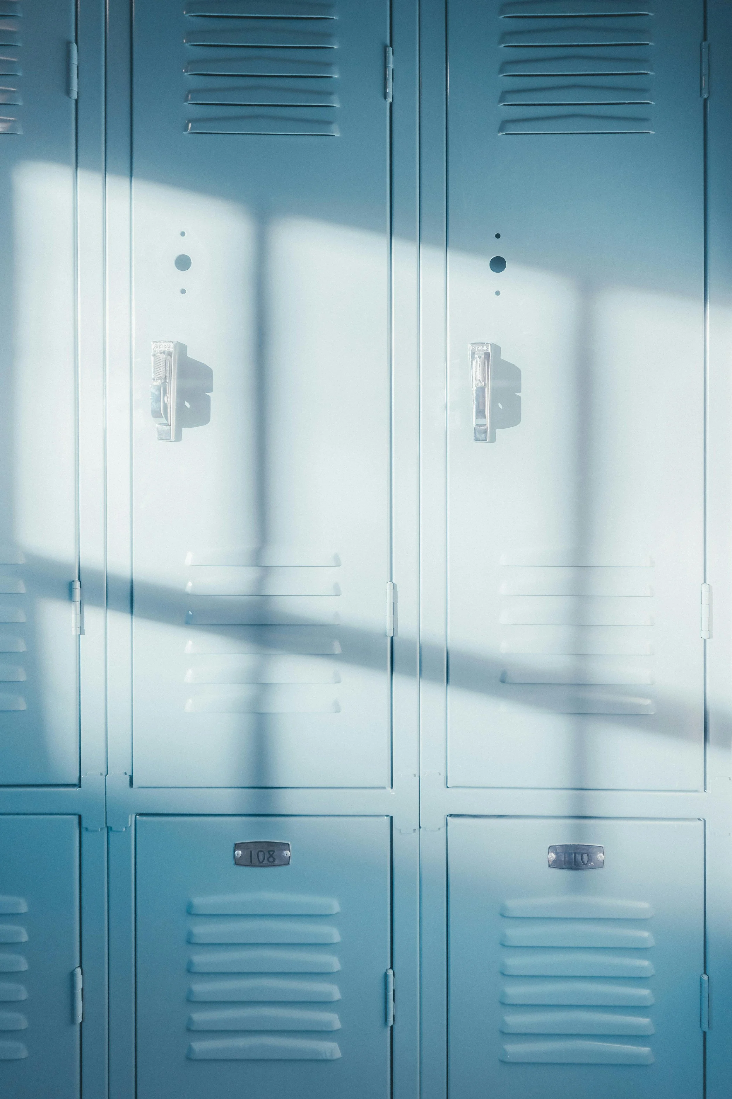 A row of light blue school lockers with shadows cast across their doors.