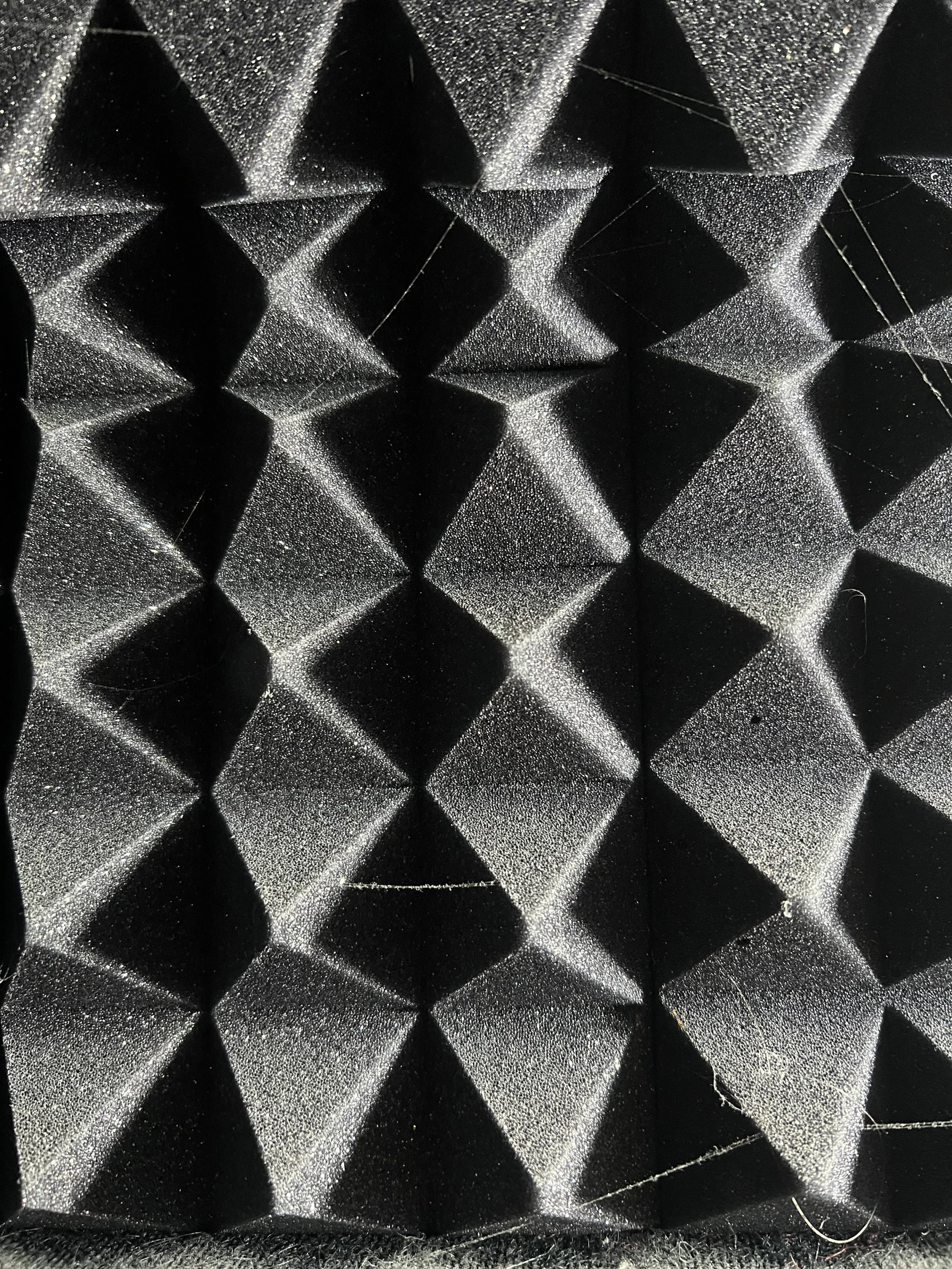 Close-up of black acoustic foam panels with a pattern of three-dimensional pyramids for sound absorption.