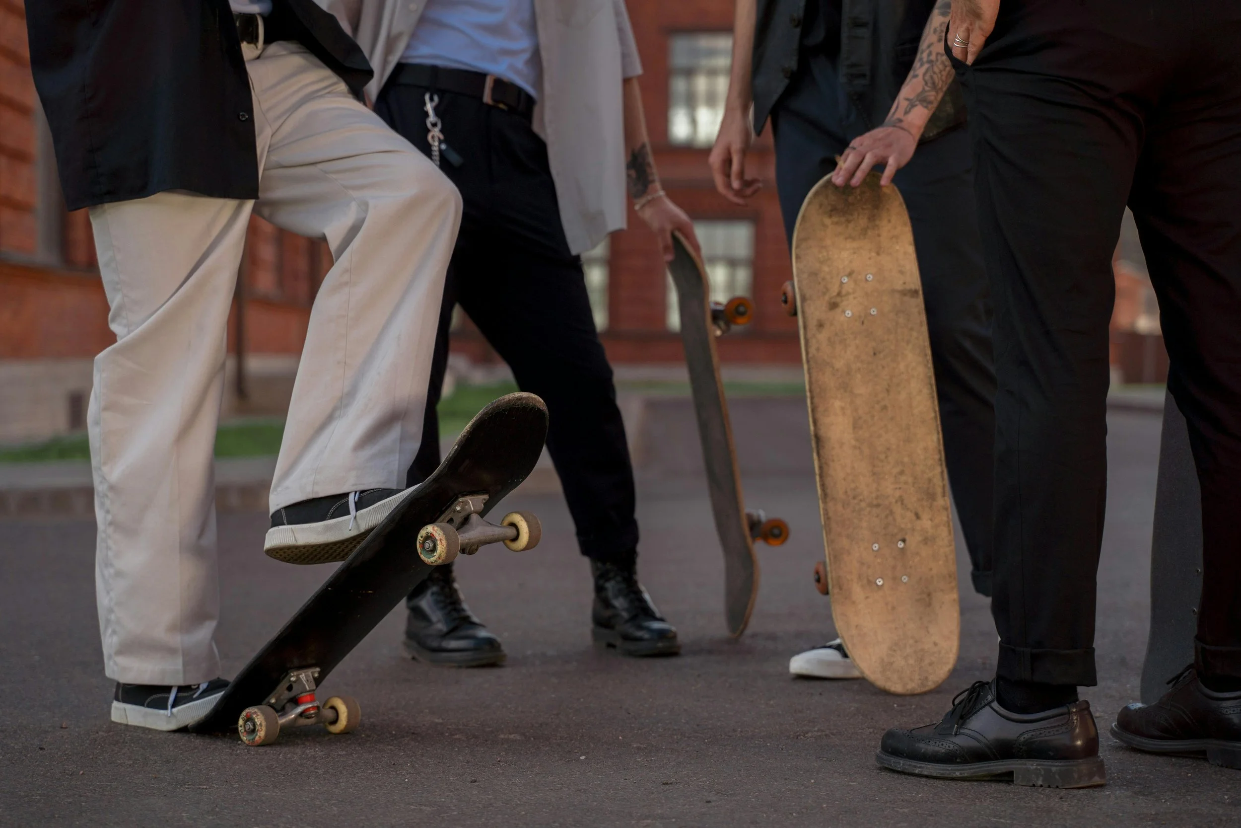 Group of four people holding skateboards, standing on pavement outside a brick building.