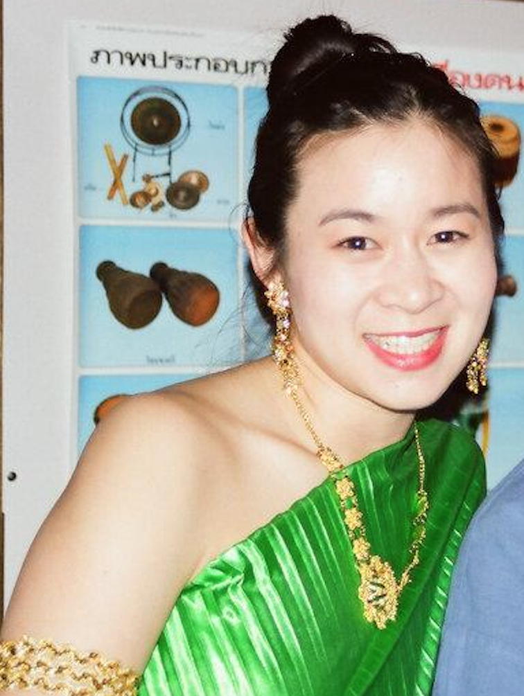 Cindy Kay wearing traditional Indian attire with gold jewelry smiling, with a poster showing musical instruments and objects in the background.