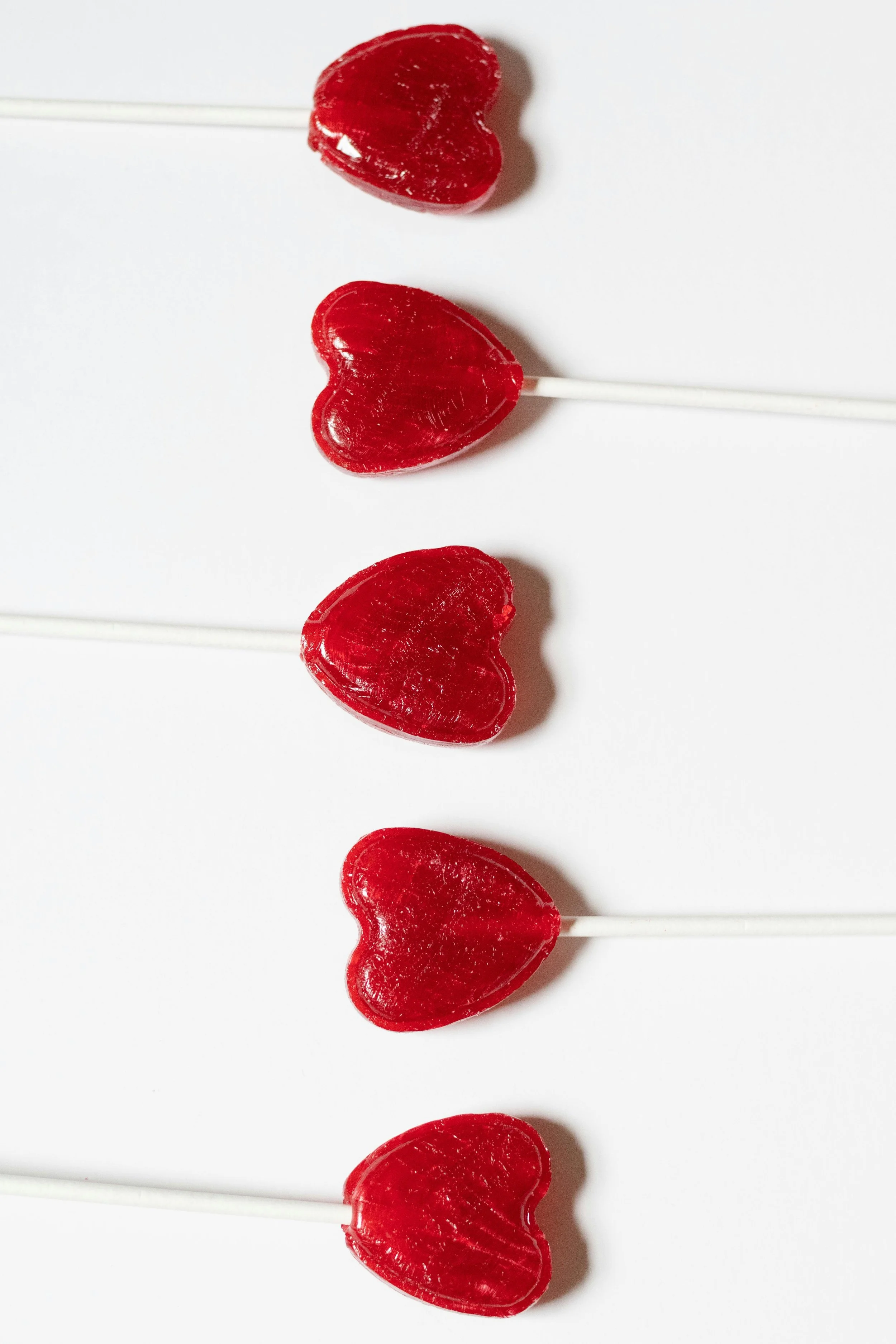 Five red heart-shaped lollipops lined up vertically against a white background.
