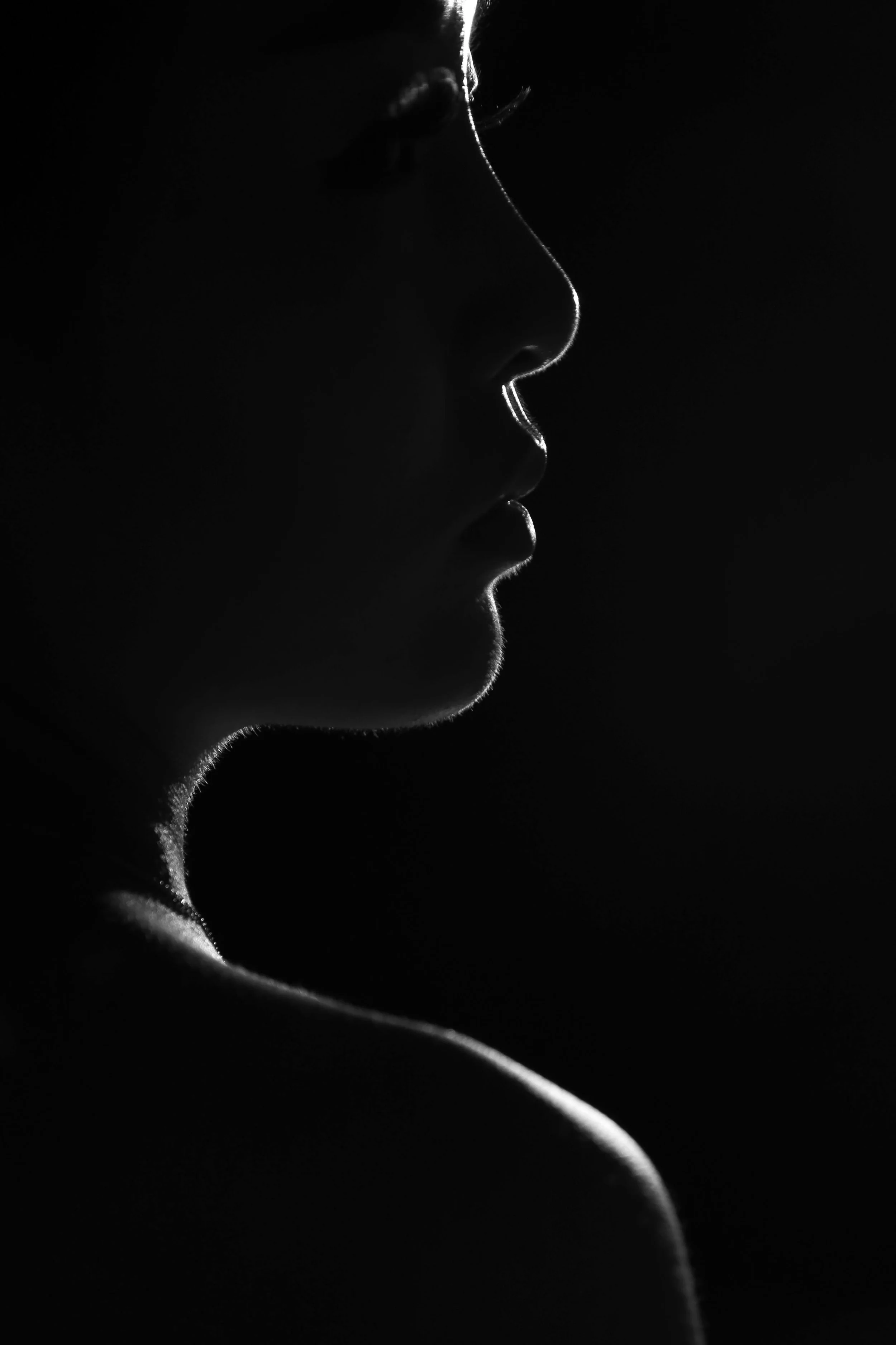 Silhouette of a woman's face and shoulder with backlighting, showing profile view in black and white.