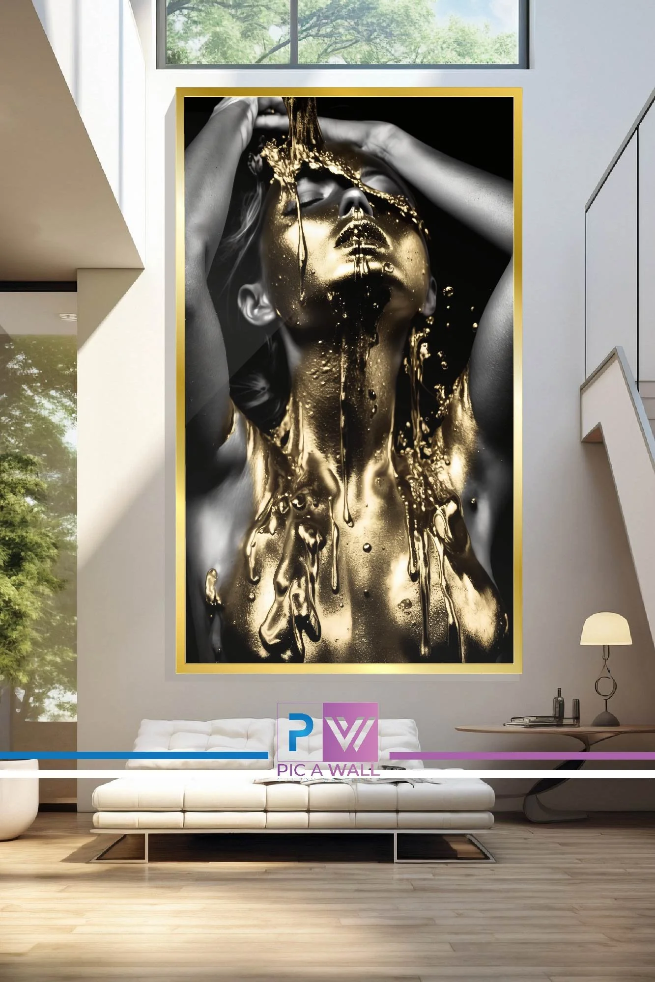 Large framed black and gold artwork of a woman with her eyes closed, metallic gold paint on her face and body, in a modern living room with white couch, desk, lamp, and large window.