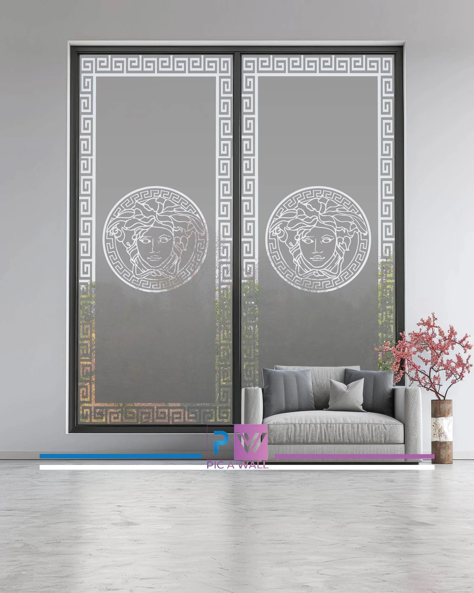 Decorative glass window with Medusa head design and Greek key border, in a modern living room with a gray sofa, pillows, and a pink flowering plant in a vase.