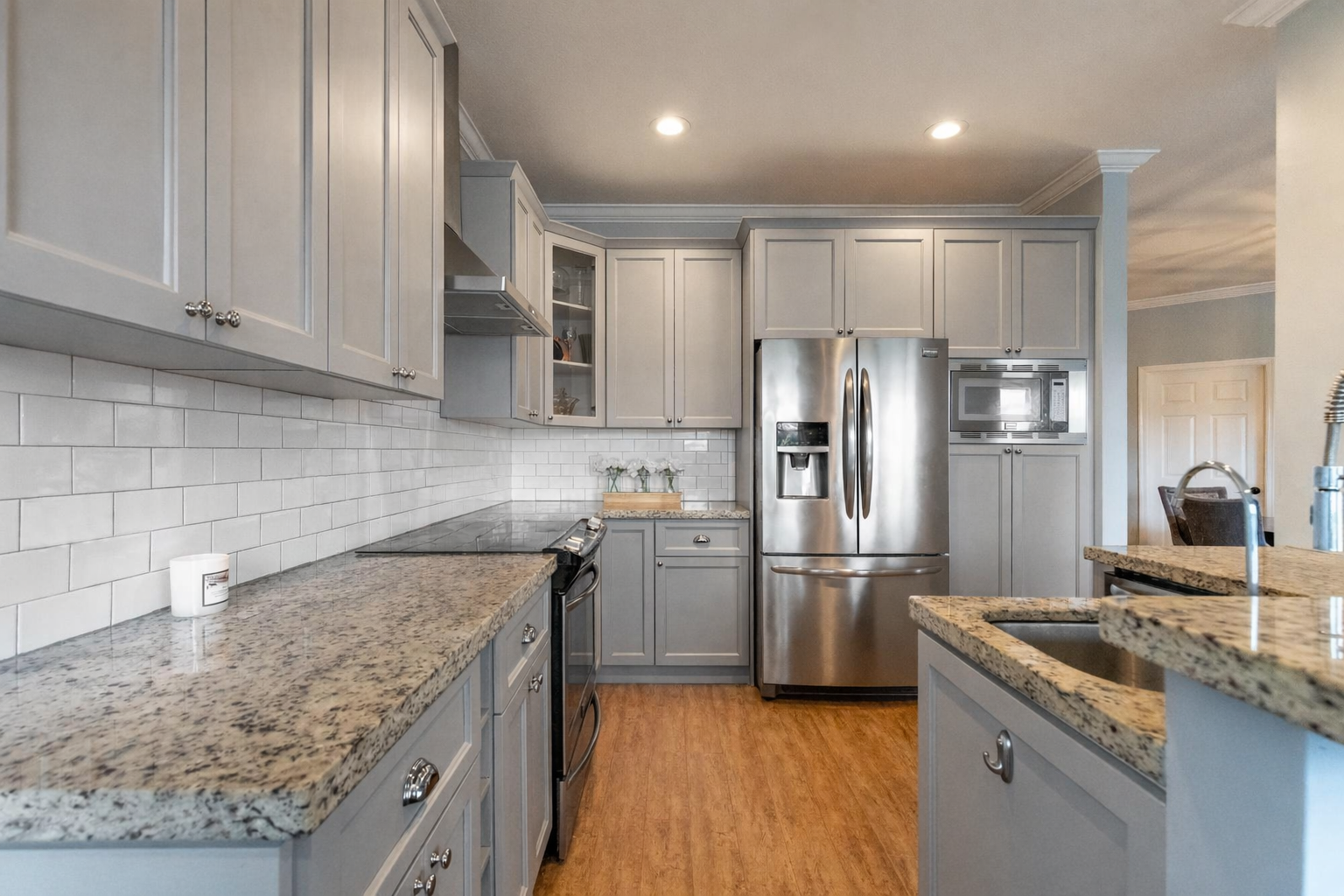 Kitchen with gray cabinets, granite countertops, white subway tile backsplash, stainless steel refrigerator, microwave, and stove, and hardwood floors.