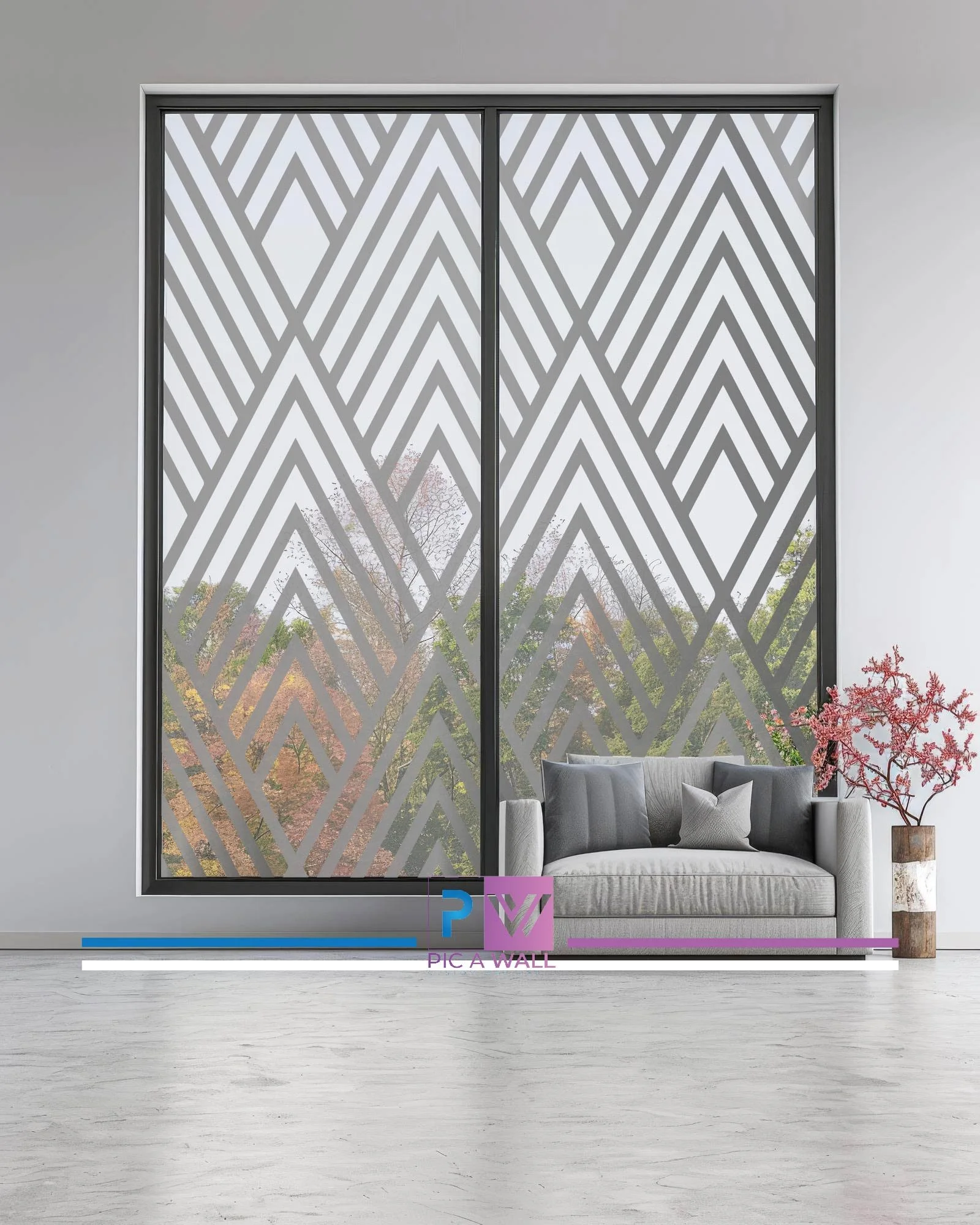 Modern living room with large window featuring a decorative geometric pattern. There is a light gray sofa with four cushions and a tall vase with a pink flowering plant beside it. The floor is white, and the wall is plain white.
