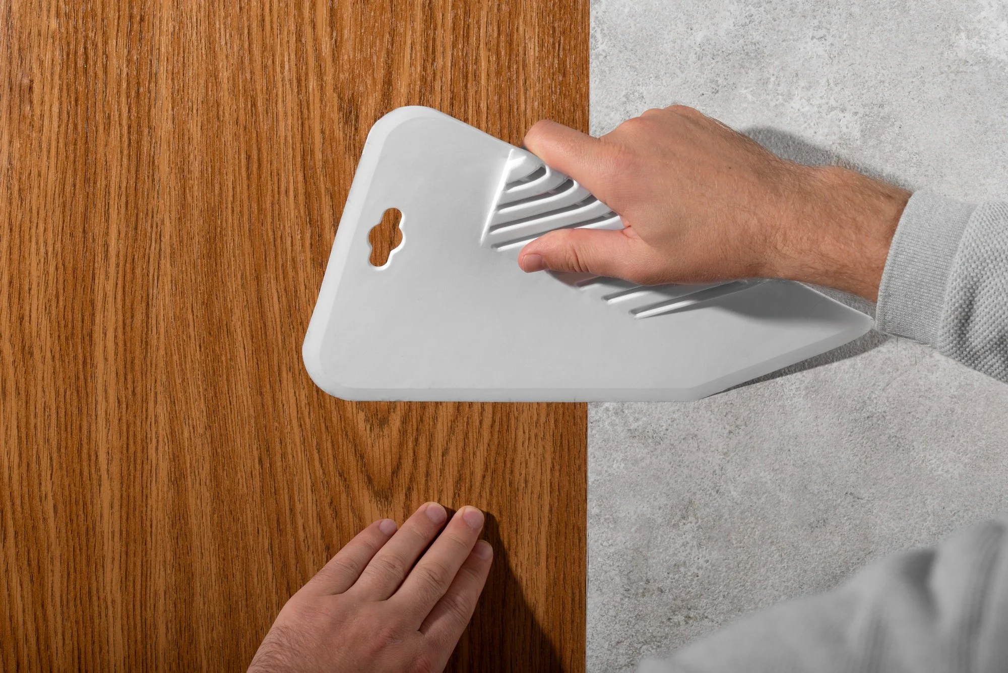 A person using a drywall sander to sand a wall, with a hand holding the sander and another hand steadying the wall.