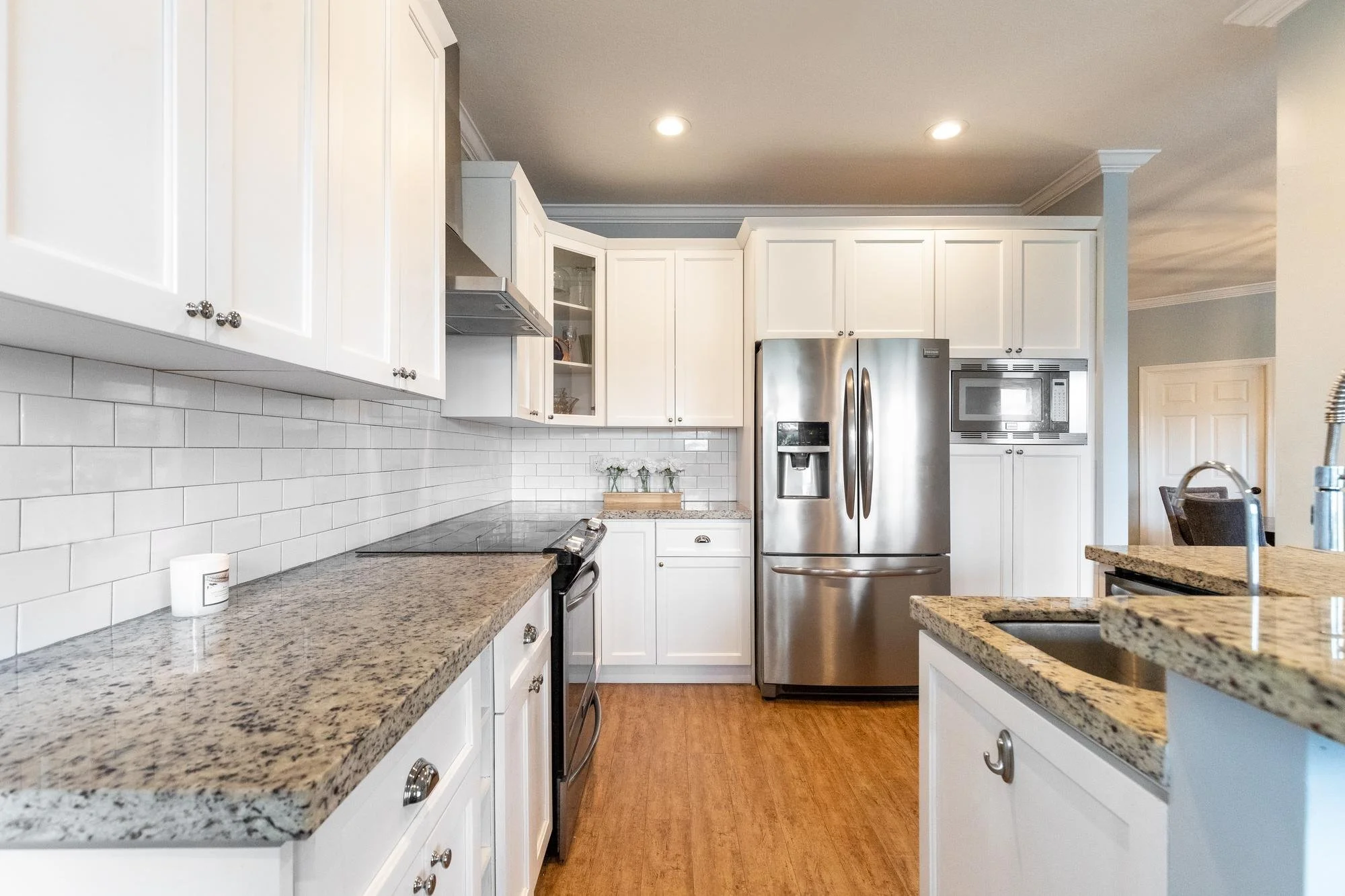Kitchen with white cabinets, beige granite countertops, stainless steel refrigerator, microwave, oven, and a blended countertop with a sink.