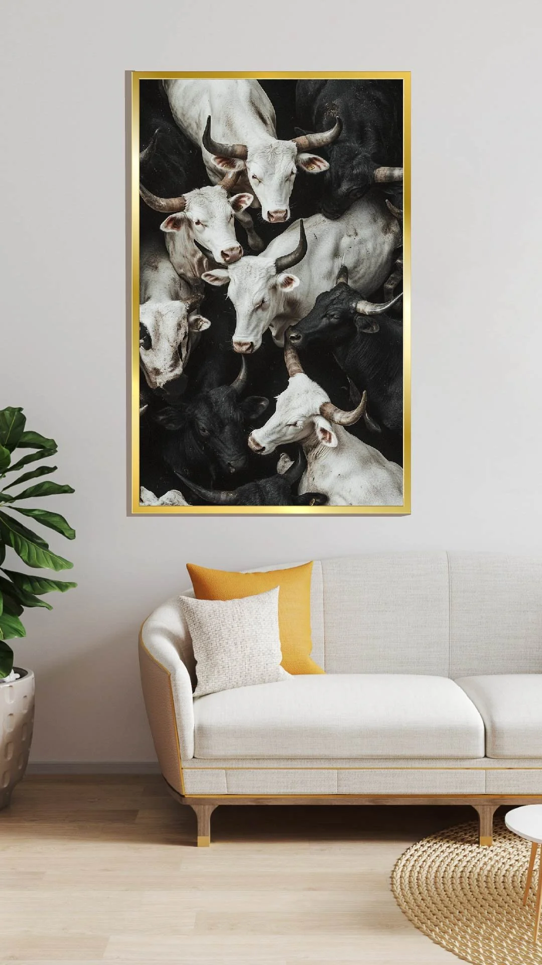 A large framed poster of a herd of cattle with white and black cows, hung on a light-colored wall above a white sofa with yellow and beige pillows, next to a green leafy plant in a white pot, in a modern living room.