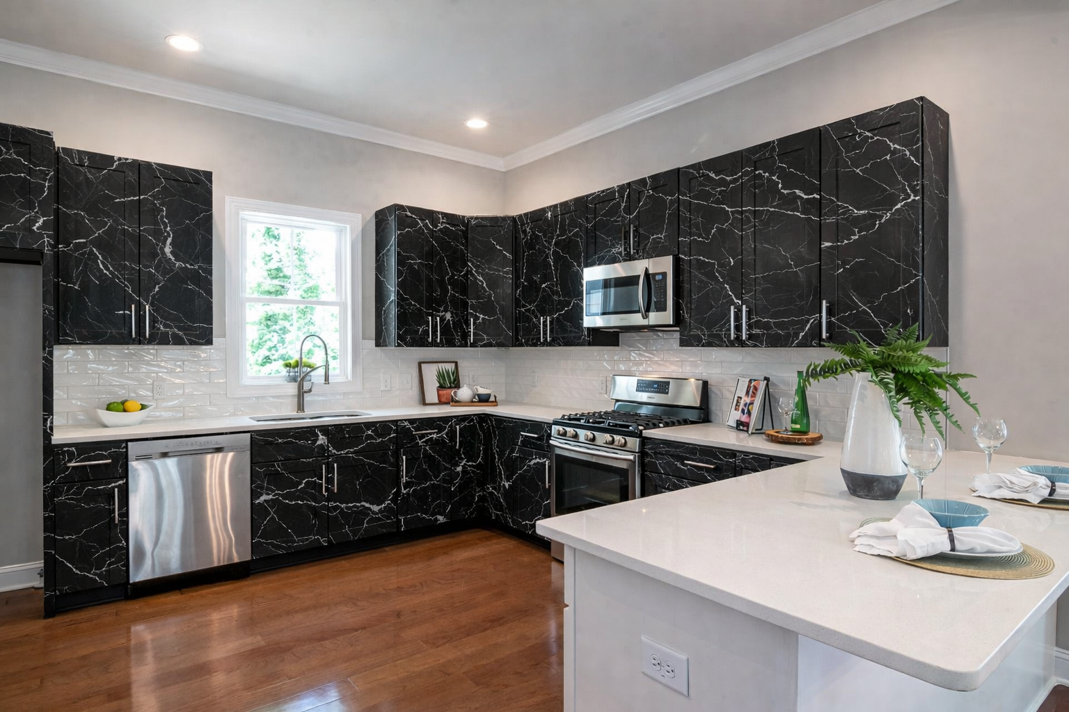 Modern kitchen with black marble cabinets, white backsplash, stainless steel appliances, and wood flooring.