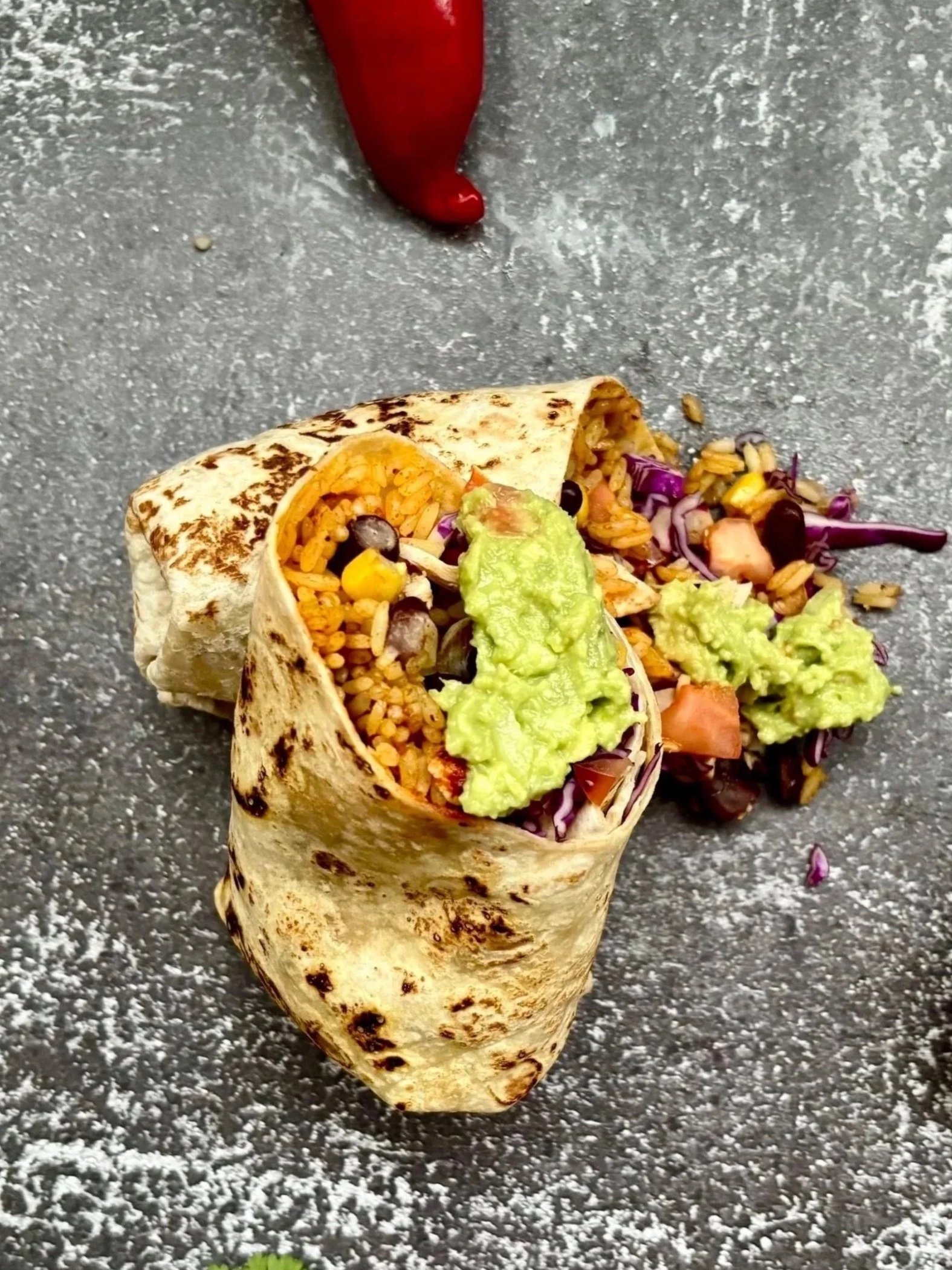 Mexicansk burrito i Aarhus med fyld af ris, sorte bønner, salat og guacamole, placeret på en grå overflade.