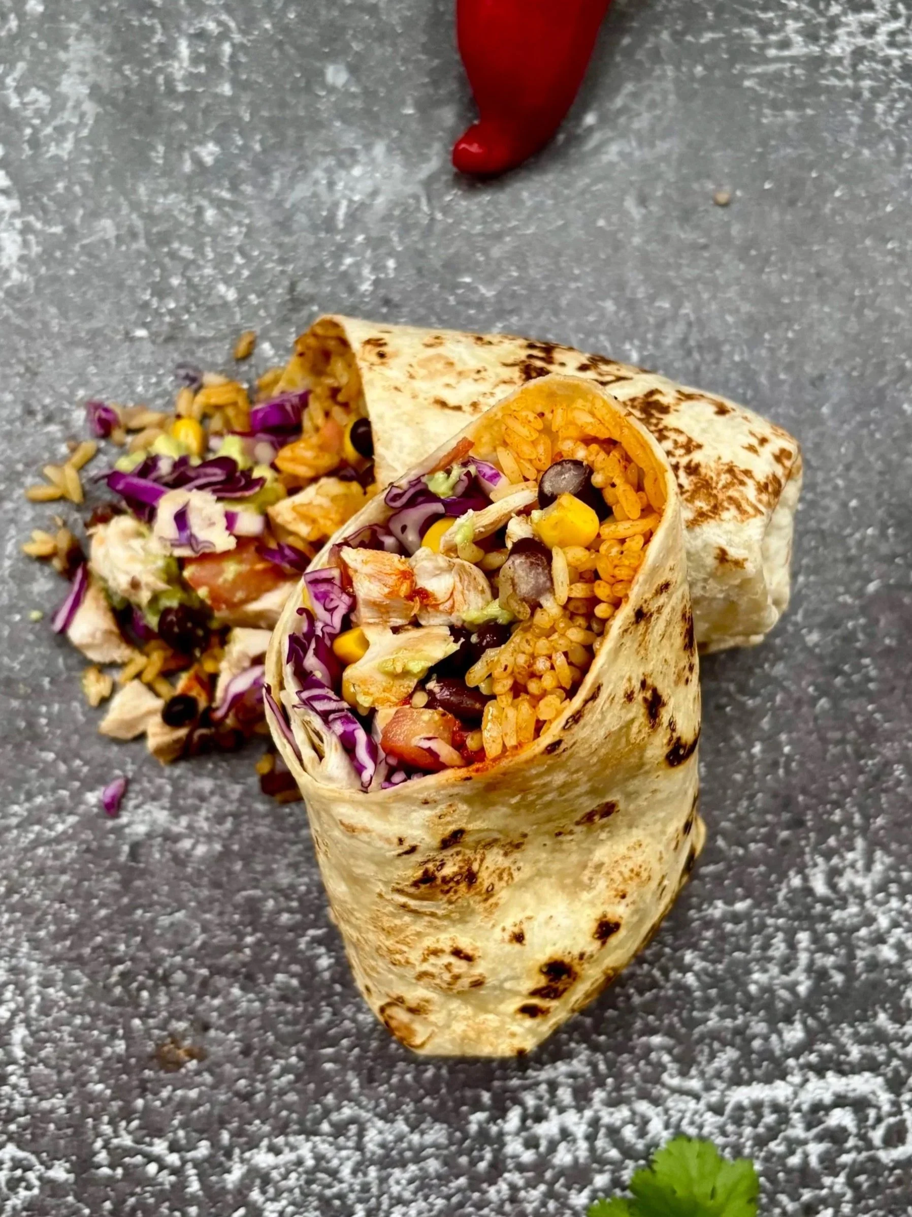 Mexicansk Taco i Aarhus fyldt med ris, bønner, majskerner, kål og kylling, placeret på en grå overflade.