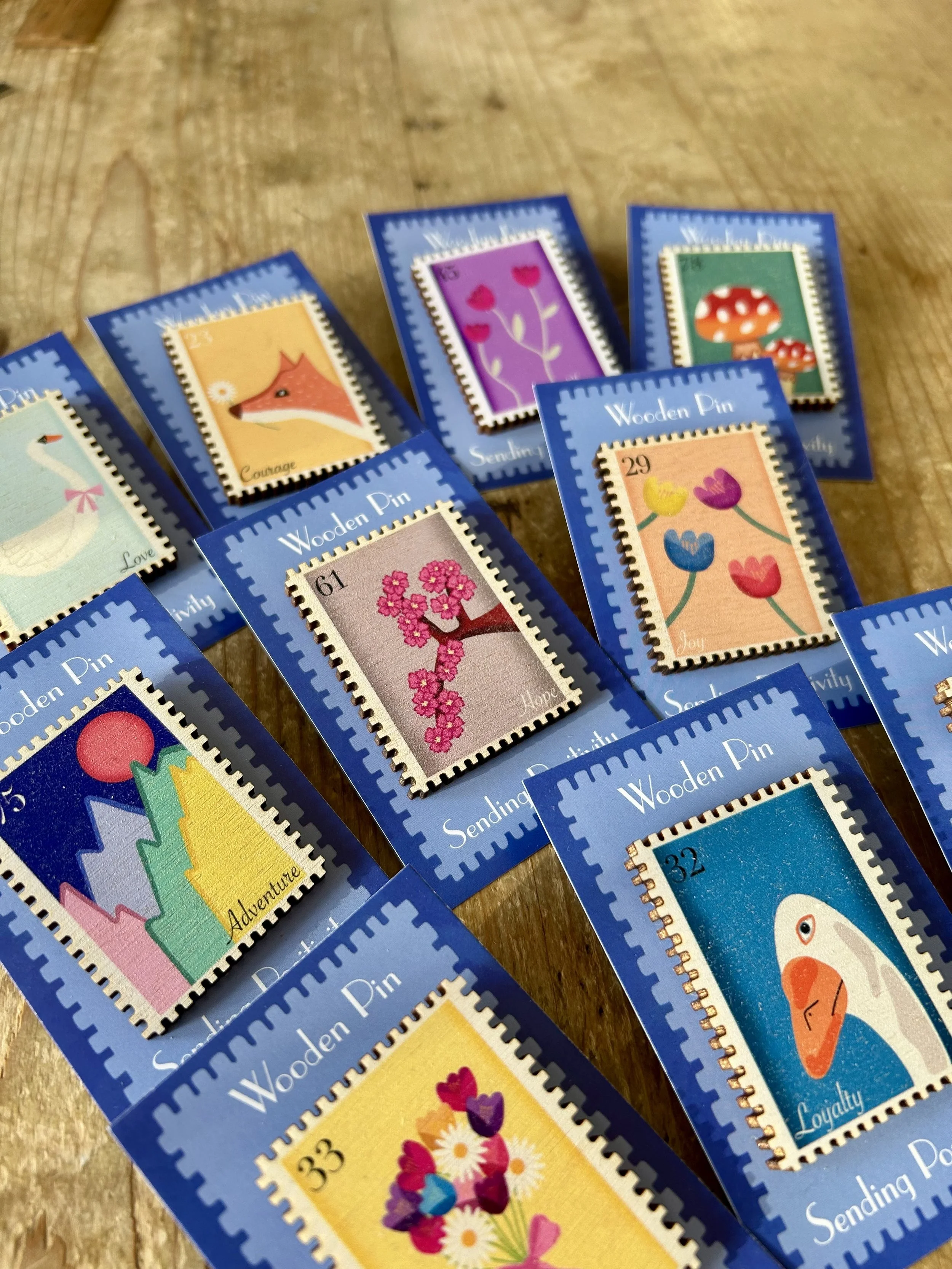 Various colorful illustrated postage stamps with floral, animal, and abstract designs, displayed on blue backing cards on a wooden surface.