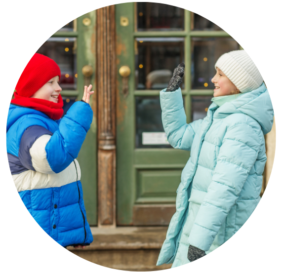 Two children in snow suits waving at eat other. 