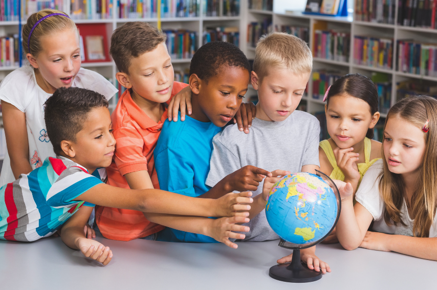 A group of children surrounding a globe in the library. Some are just looking while others are pointing at different areas. 