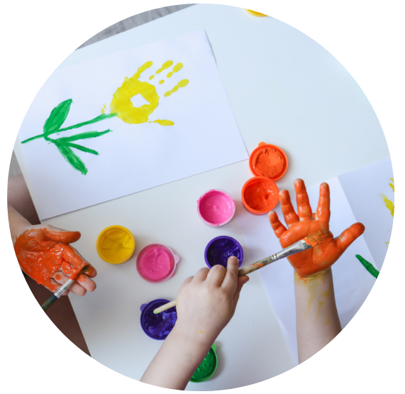 A young child is painting their hands with orange paint. Ty are making painted handprint flowers.