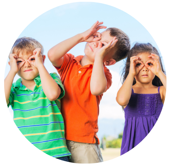 Three children making goggles with their hands. They  are outside.