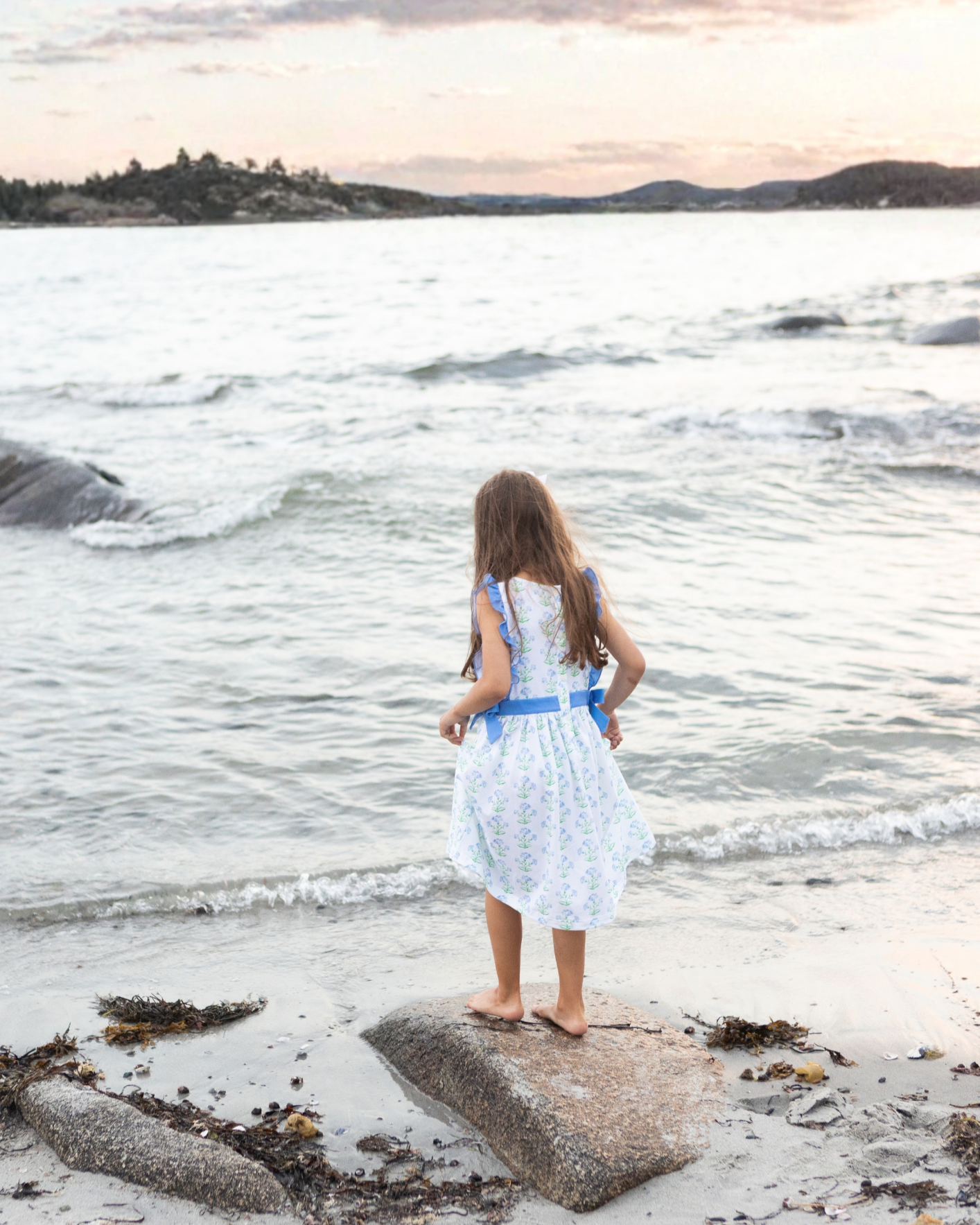Young girl standing by the ocean in Maine, looking at the waves