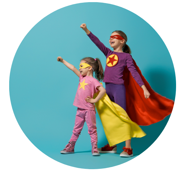 Two girls, one older and one younger, are standing in a super hero pose. They are wearing a cape and eye mask. The older girl is wearing a red cape and mask, and the younger girl is wearing a yellow cape and mask