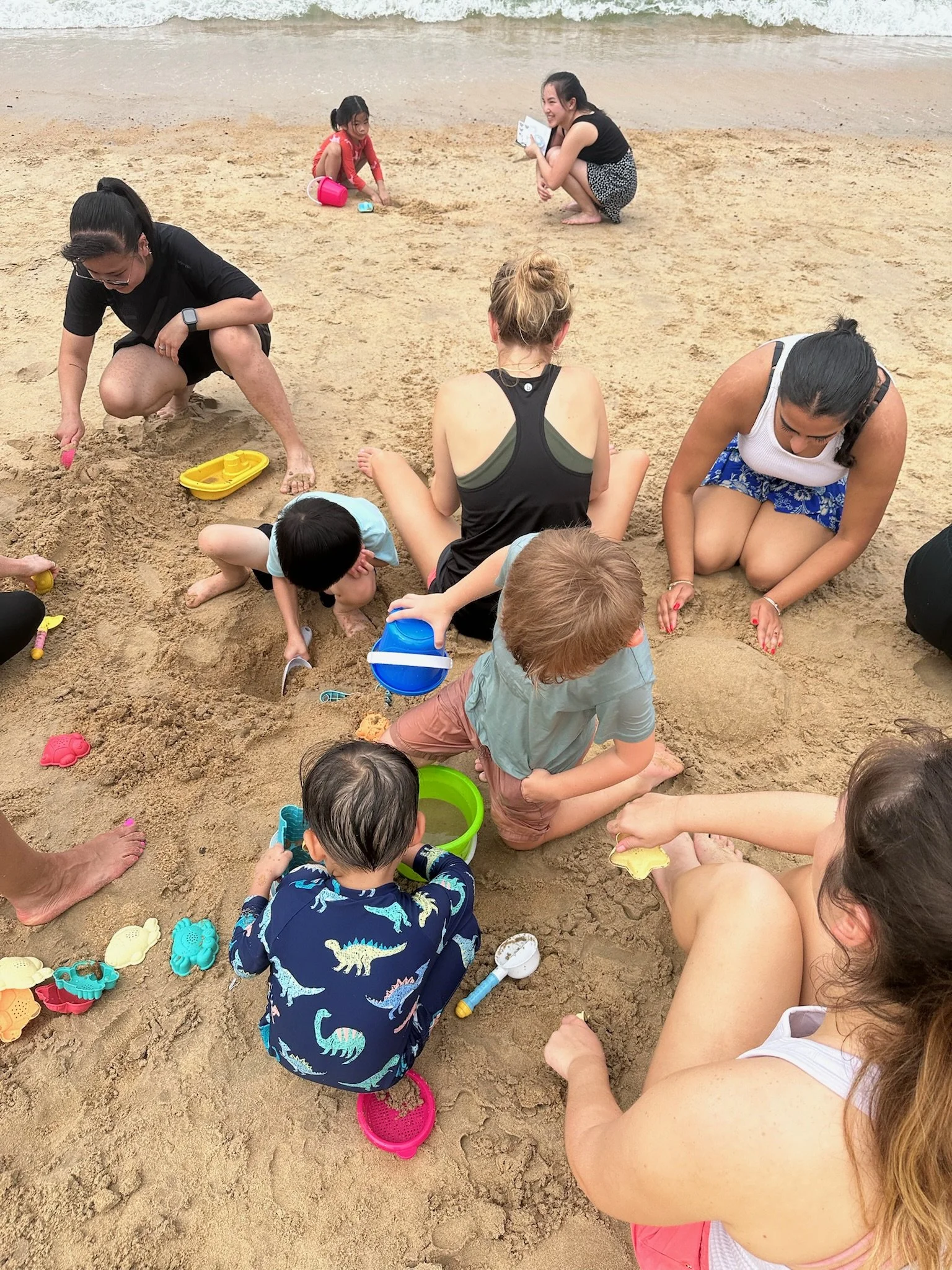 Children and adults playing and digging in the sand on a beach.