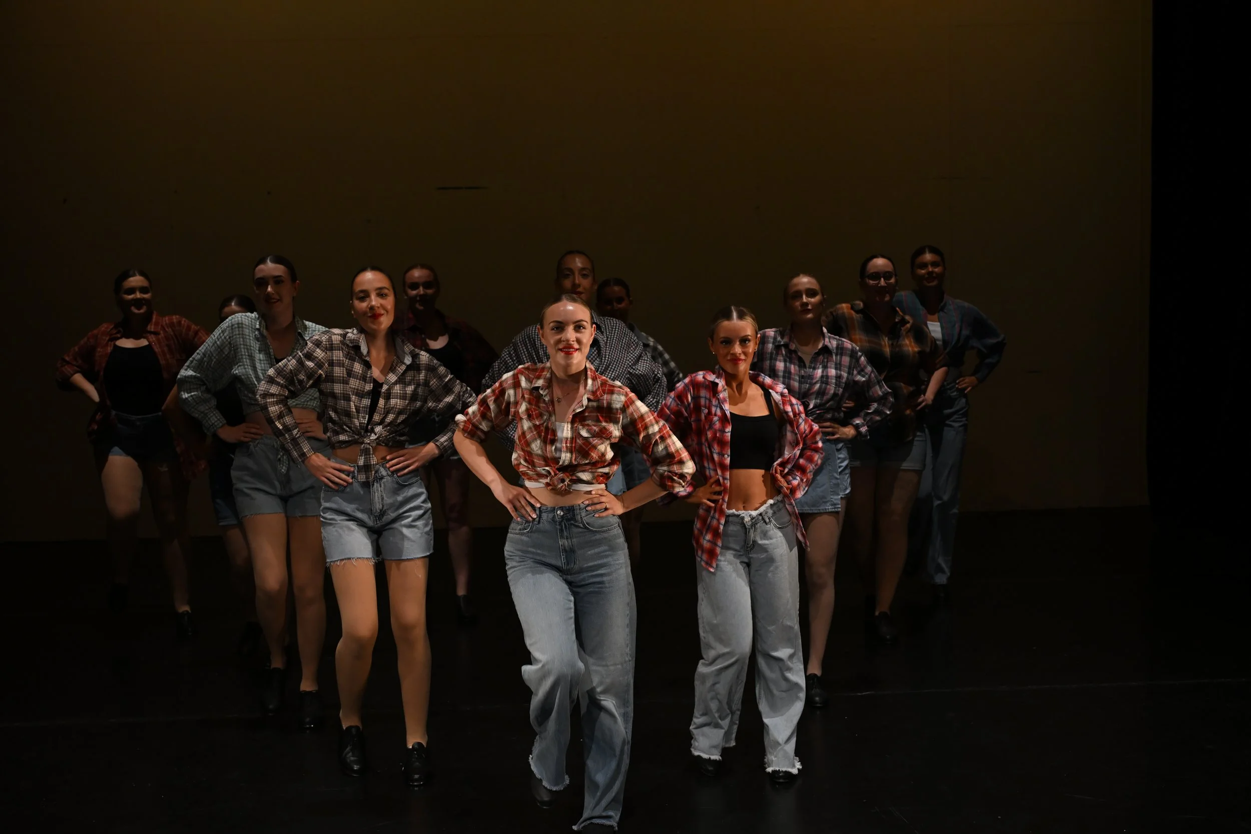 Group of women dressed in 1950s-style dance costumes on stage, posing with hands on hips.